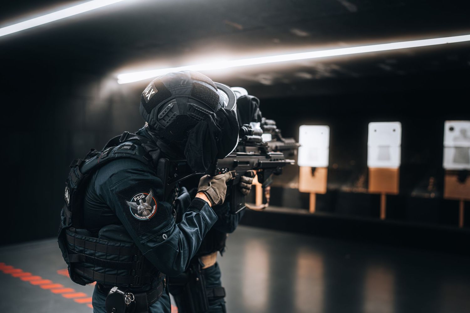 Tactical police officer in full gear aiming rifle at shooting range during training session.