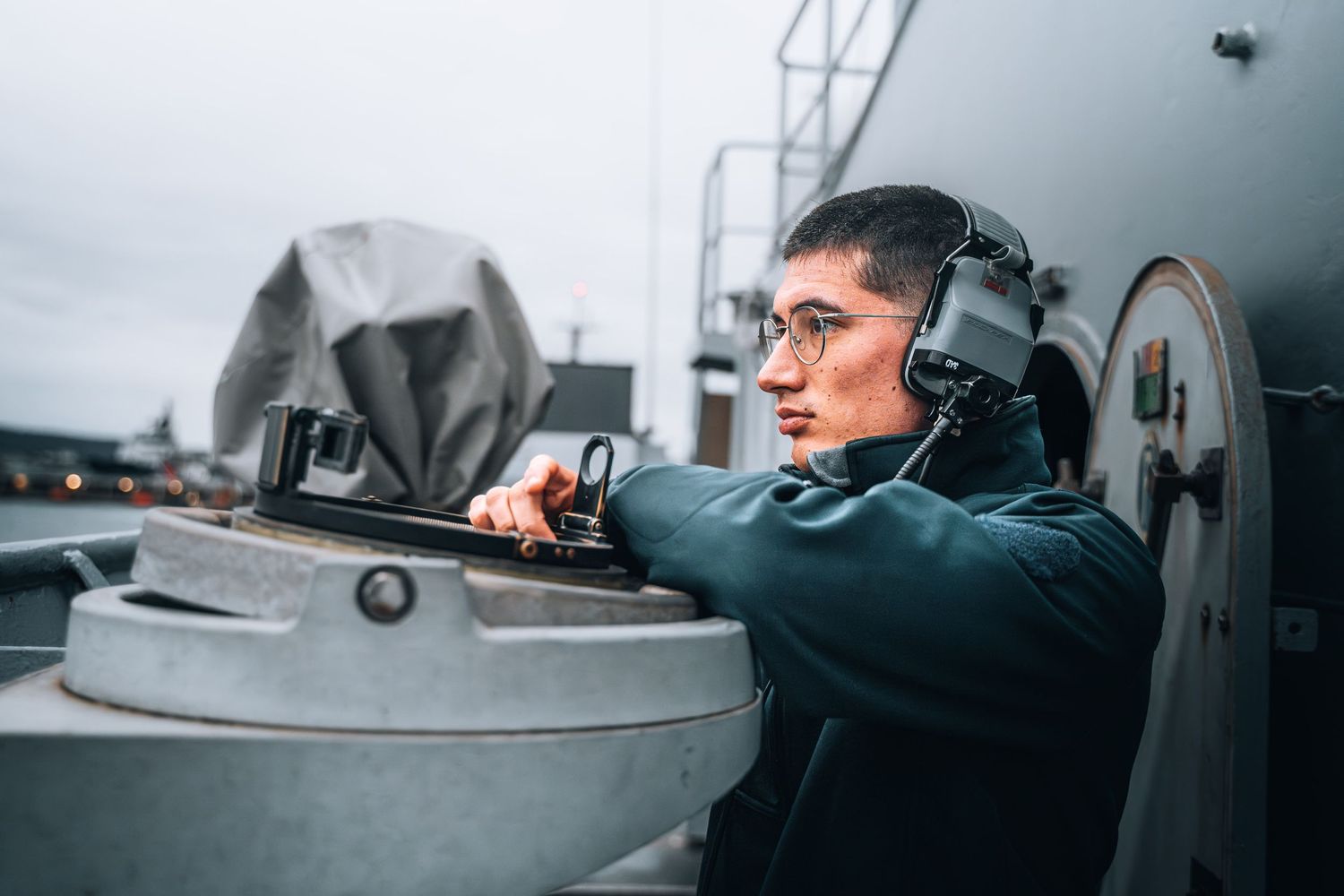 Navy sailor wearing headphones operating equipment on warship deck during maritime mission.