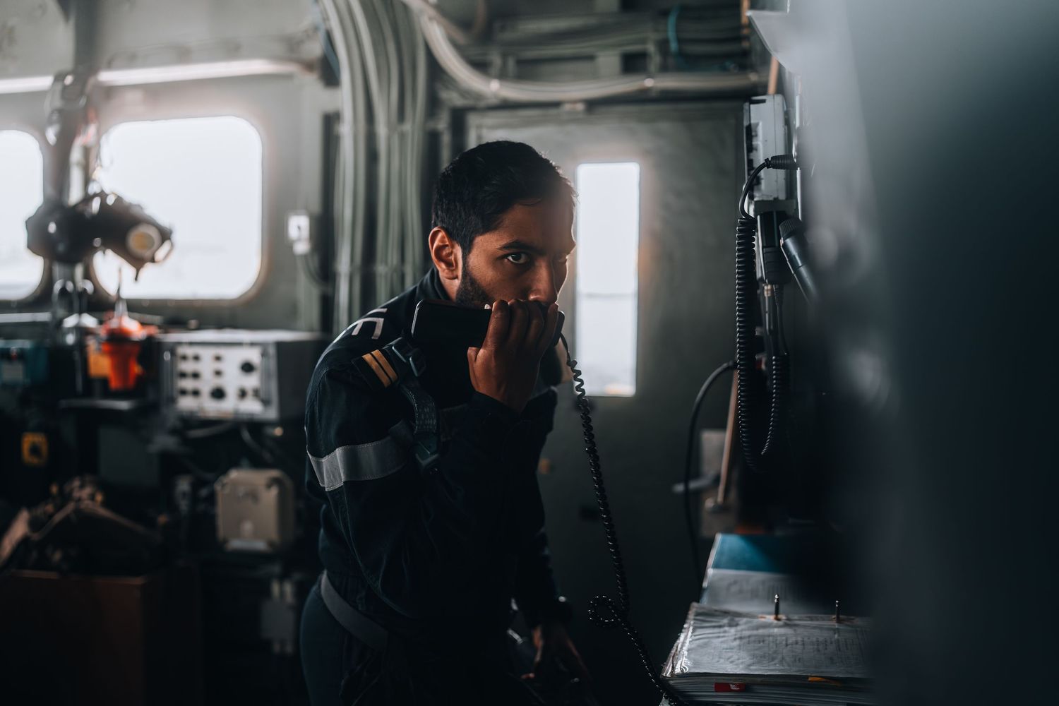 Male crew member in uniform working in a dimly lit ship engine room.