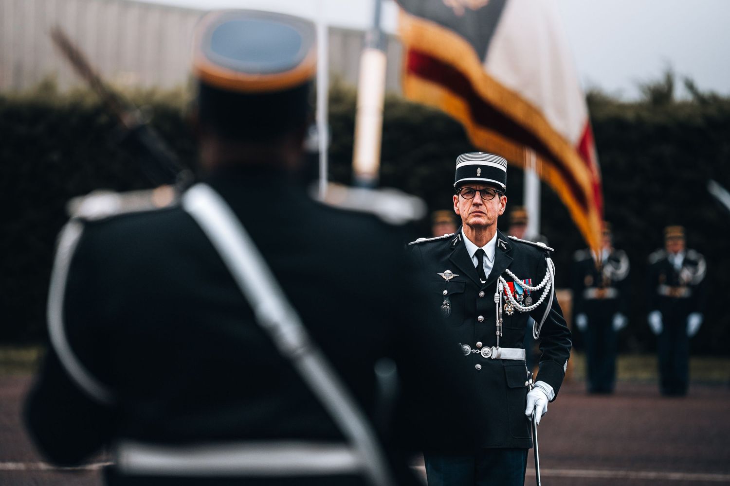 A French gendarmerie officer in dress uniform commands attention during an outdoor military parade ceremony.