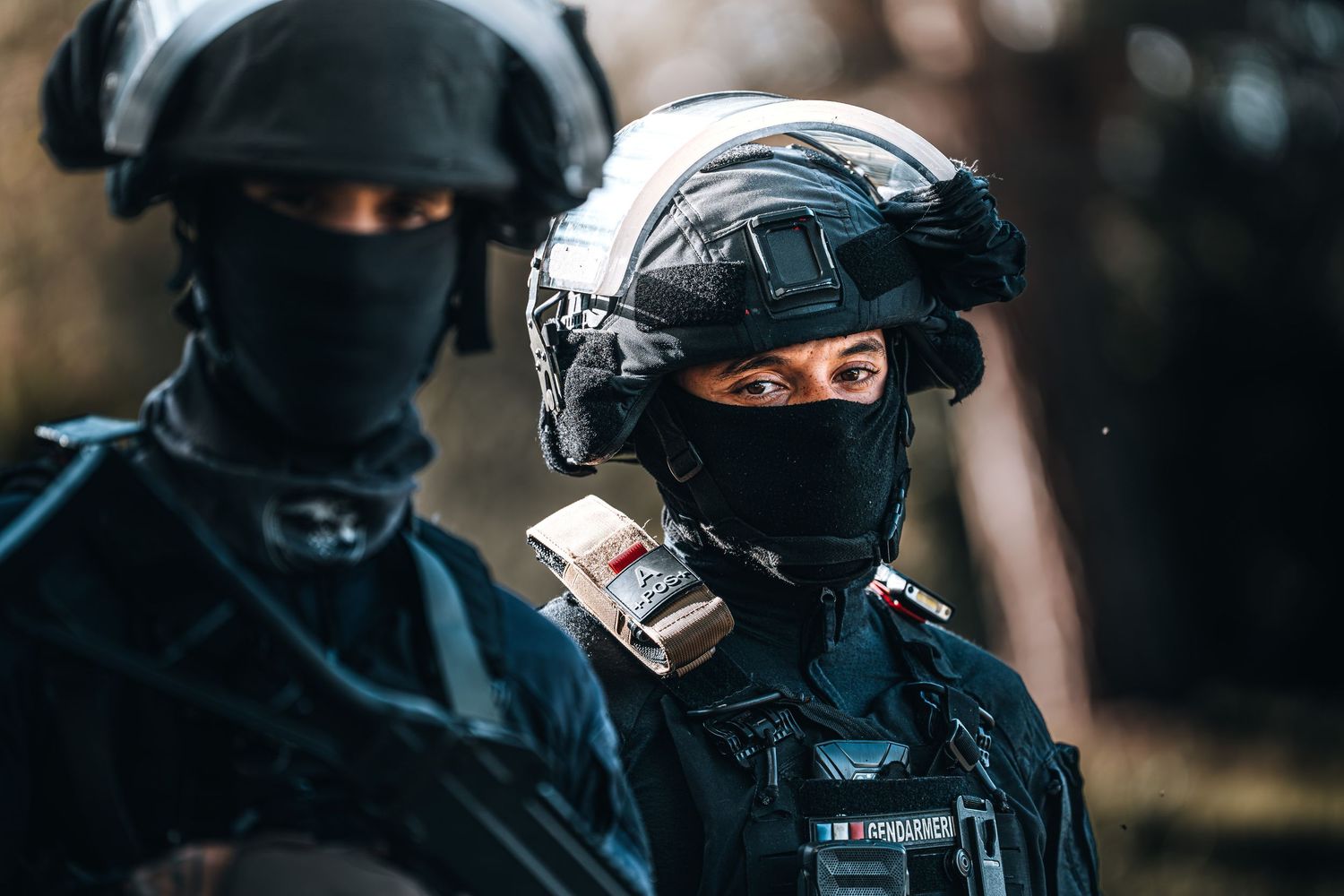 Two French Gendarmerie officers in black tactical helmets and masks during outdoor operation.