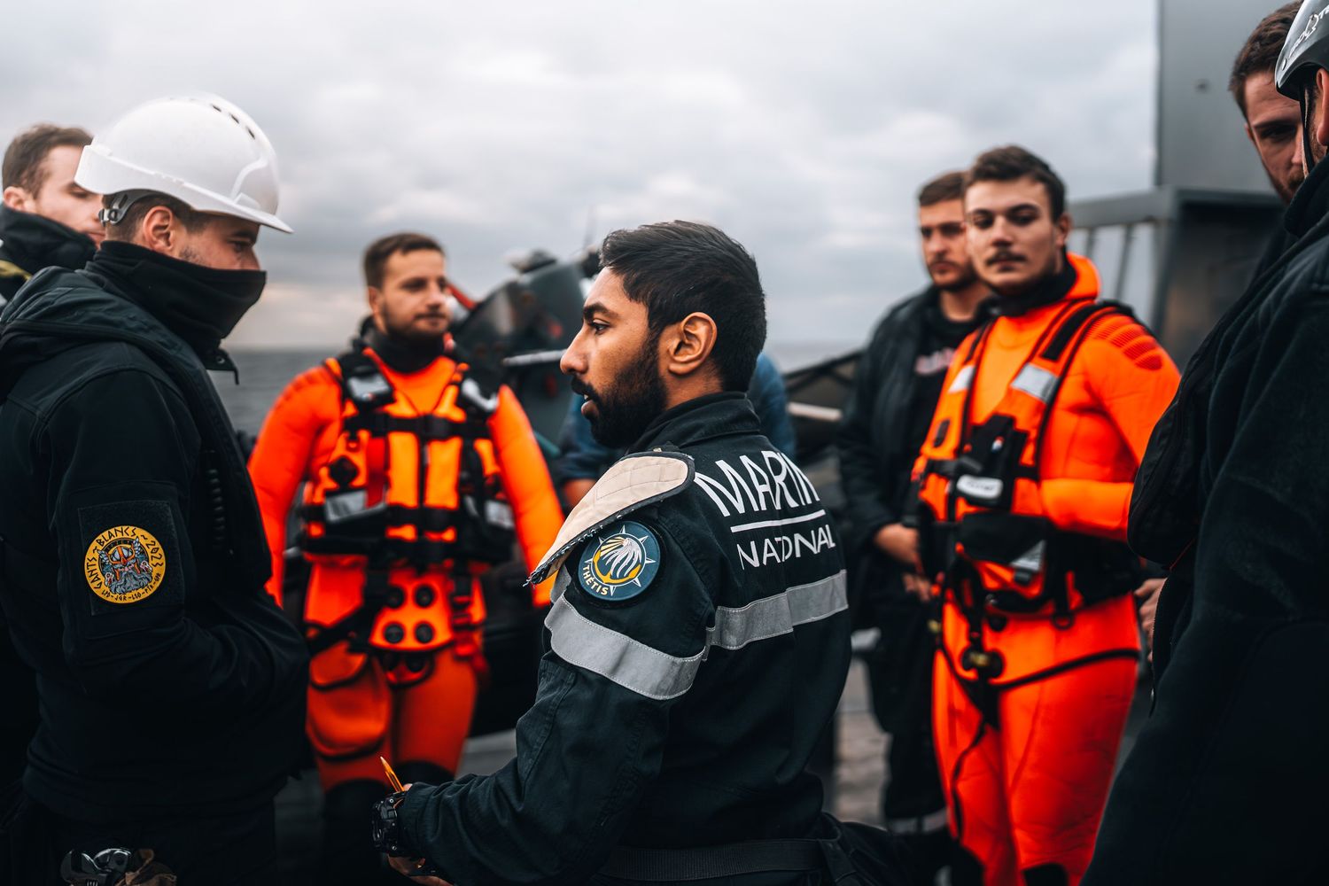 Maritime crew in safety gear having briefing on ship deck in overcast weather.