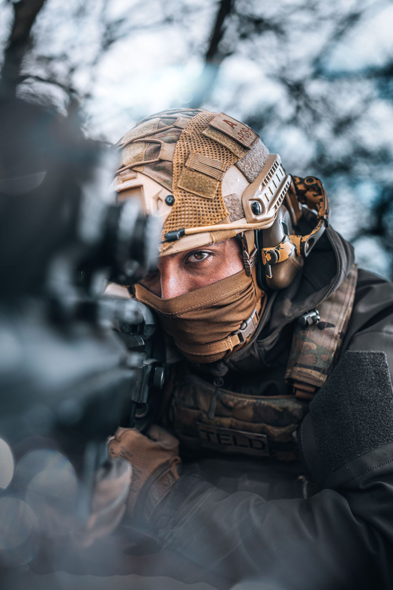 Tactical soldier in helmet and face mask aiming rifle in outdoor combat training.