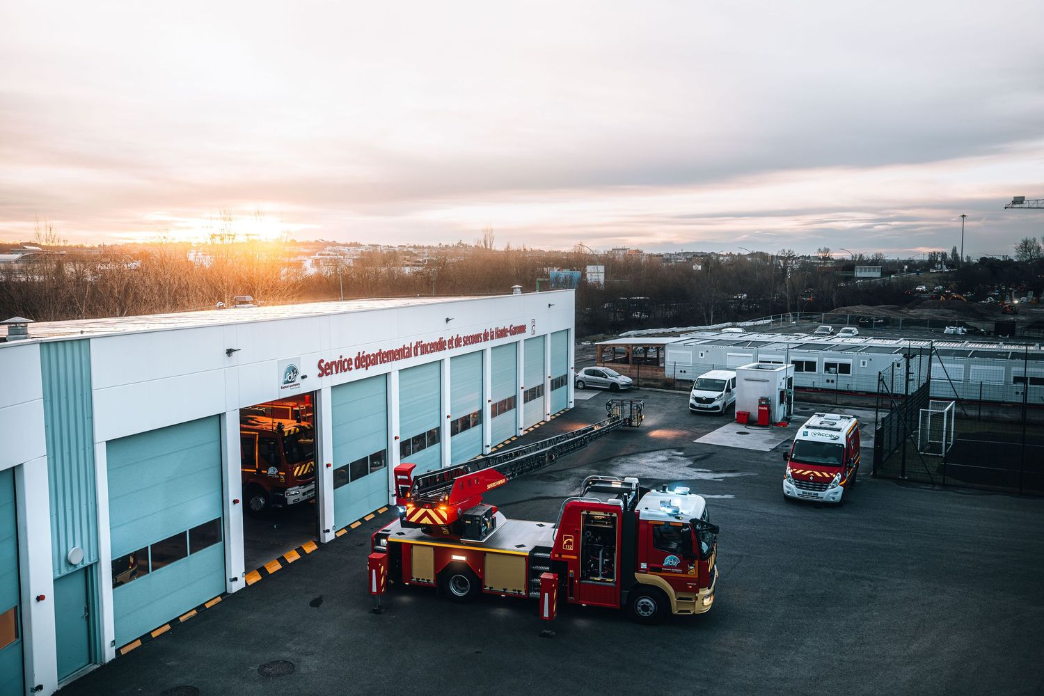 Aerial view of a French fire station with multiple red fire trucks at sunrise.
