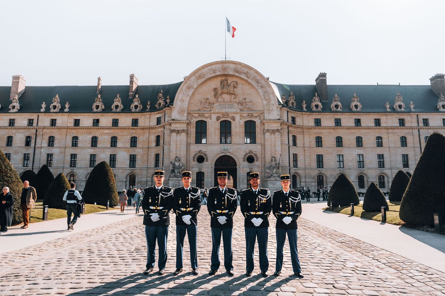 Five French gendarmerie officers in dress uniform stand at attention before the Les Invalides monument in Paris.