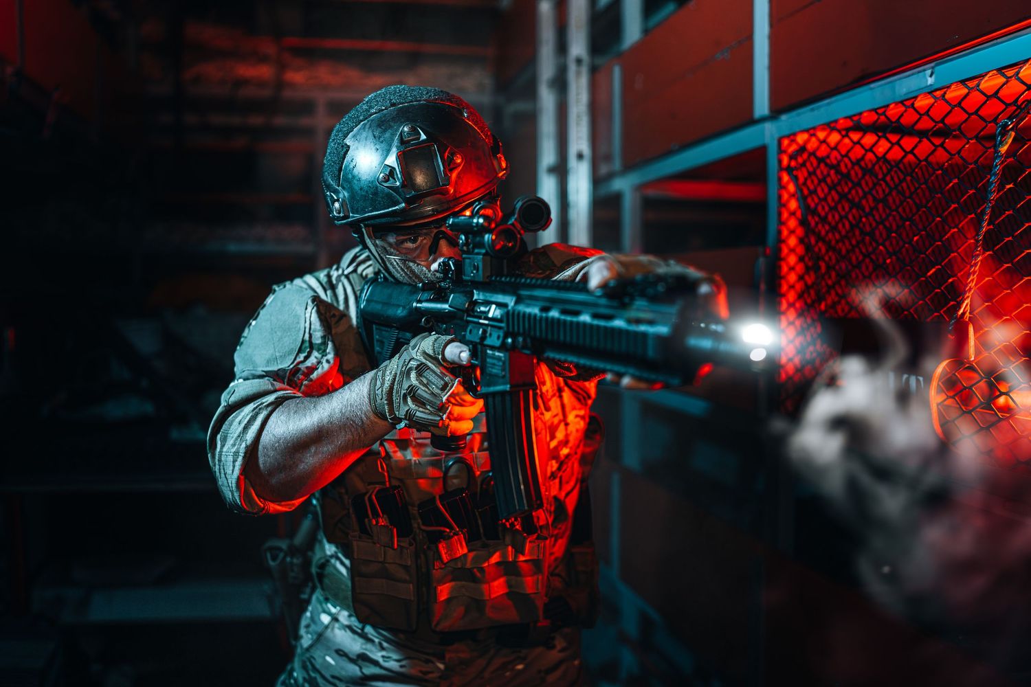 Armed soldier in tactical gear aims rifle with flashlight through red-lit smoky urban environment at night.