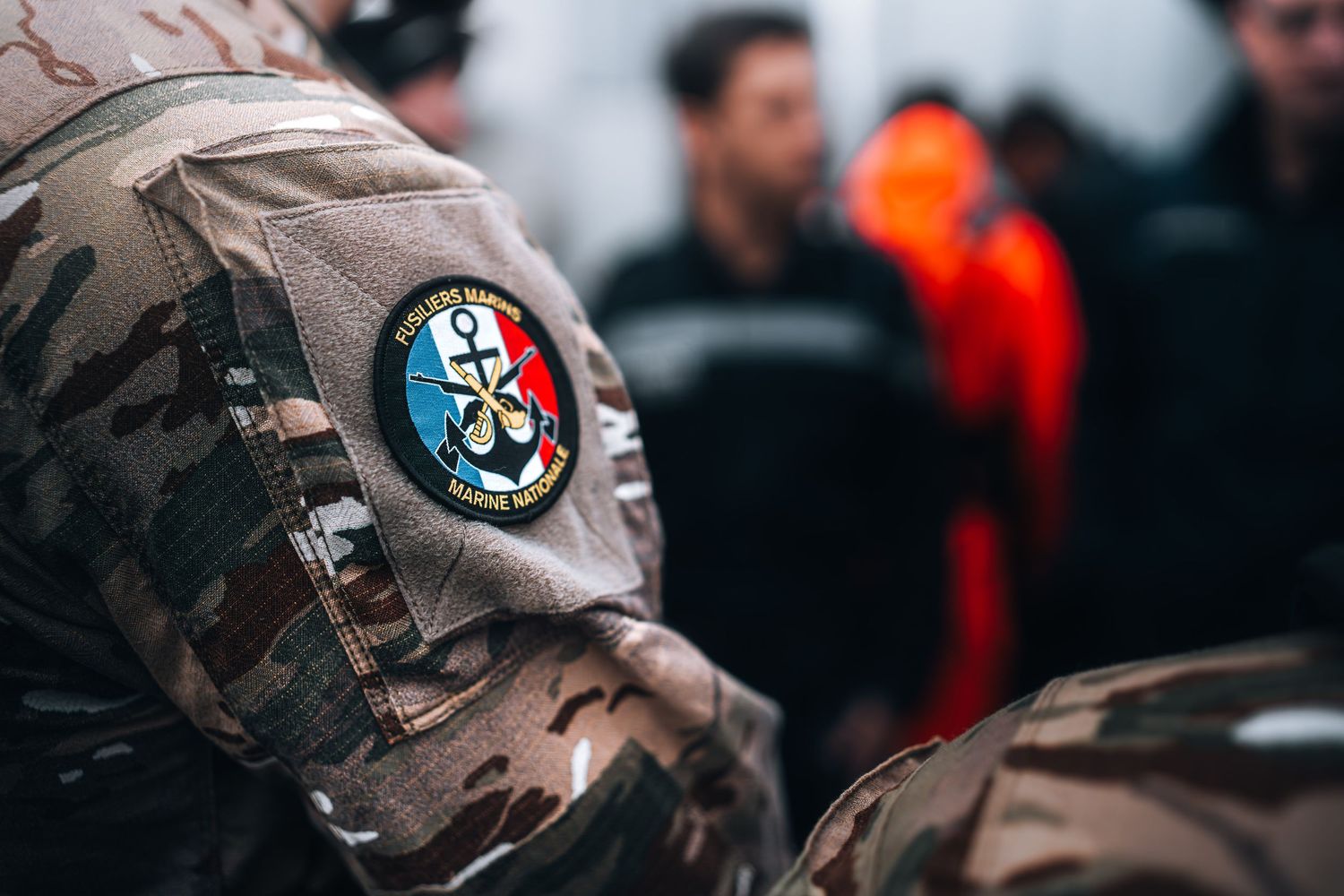 Close-up of French military camouflage uniform sleeve patch during joint naval operation briefing.