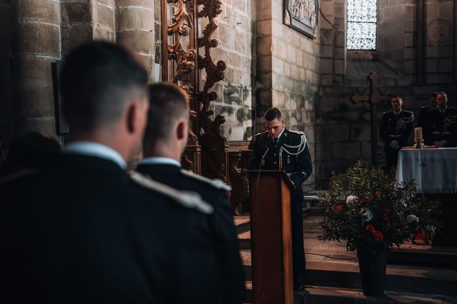 Military officer delivering a speech at a podium inside a historic stone church during a ceremony.