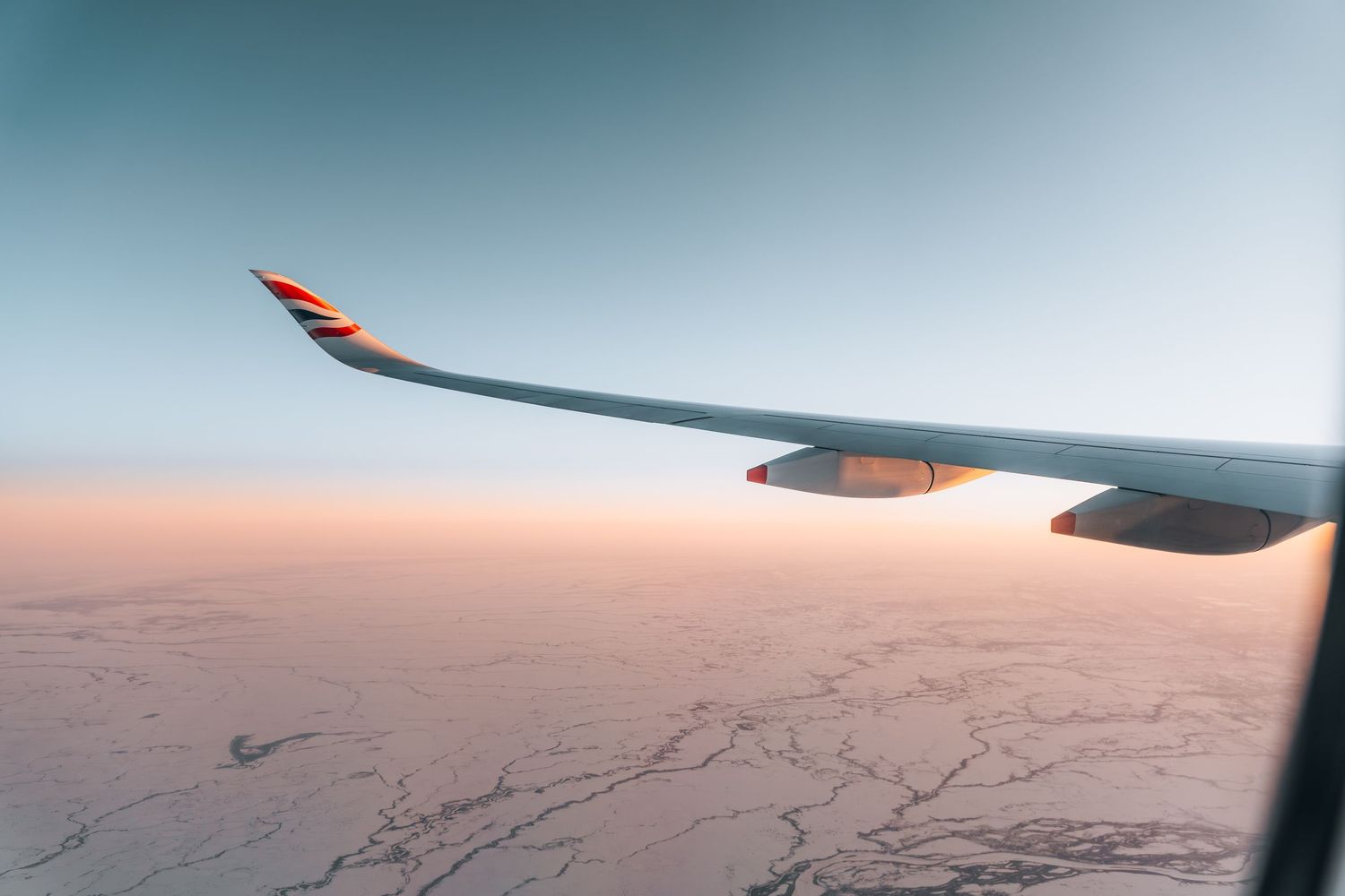 British Airways airplane wing over snowy winter landscape during warm golden sunset light.