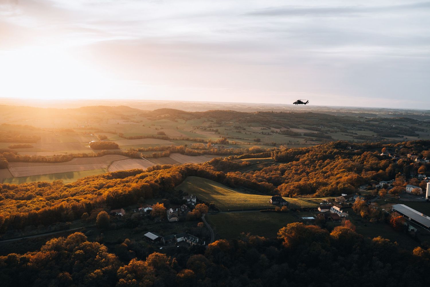 Aerial sunset view of helicopter flying over lush green countryside and small village.