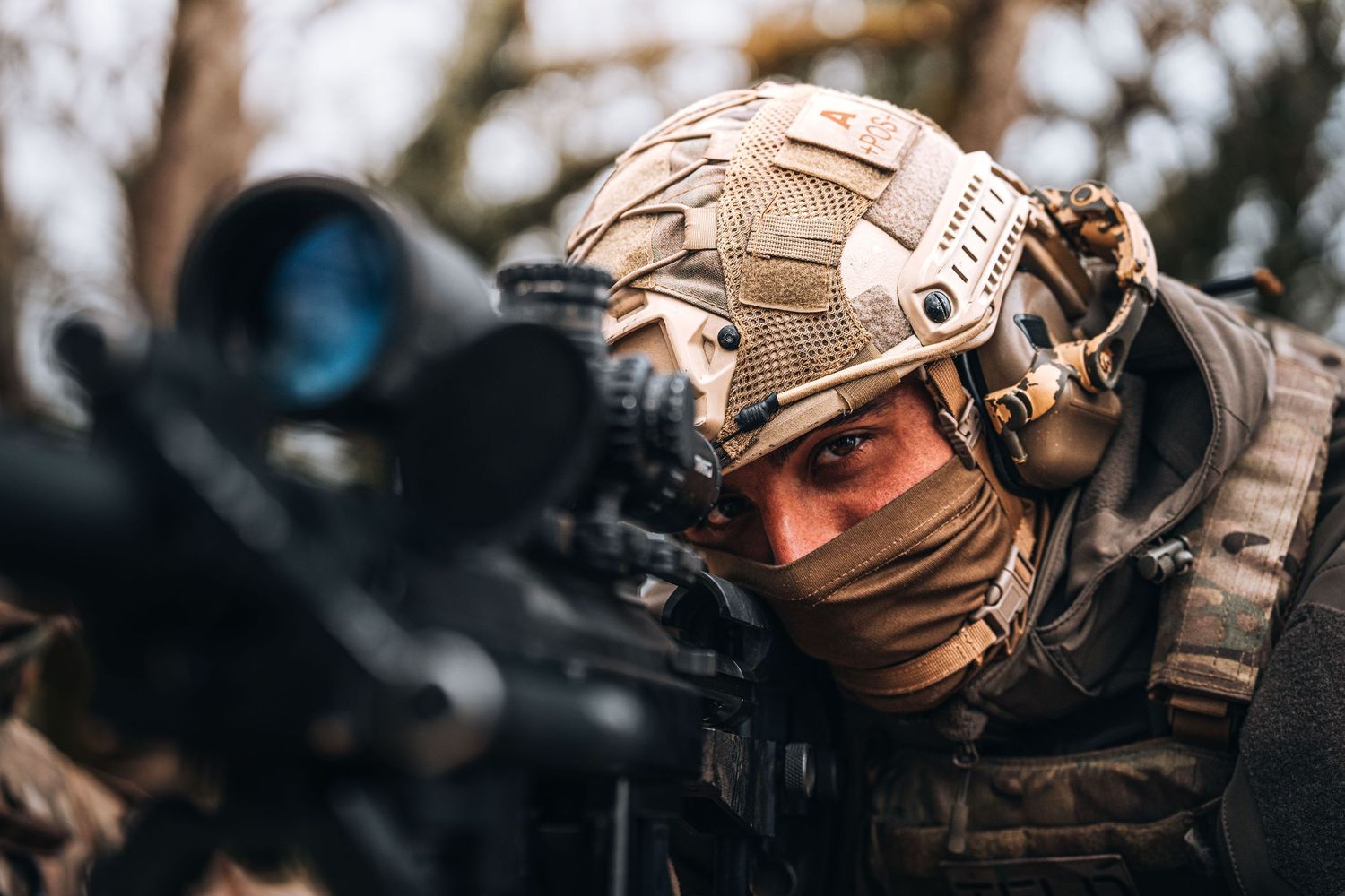 Military soldier in tactical gear aiming sniper rifle with scope in outdoor combat training exercise.