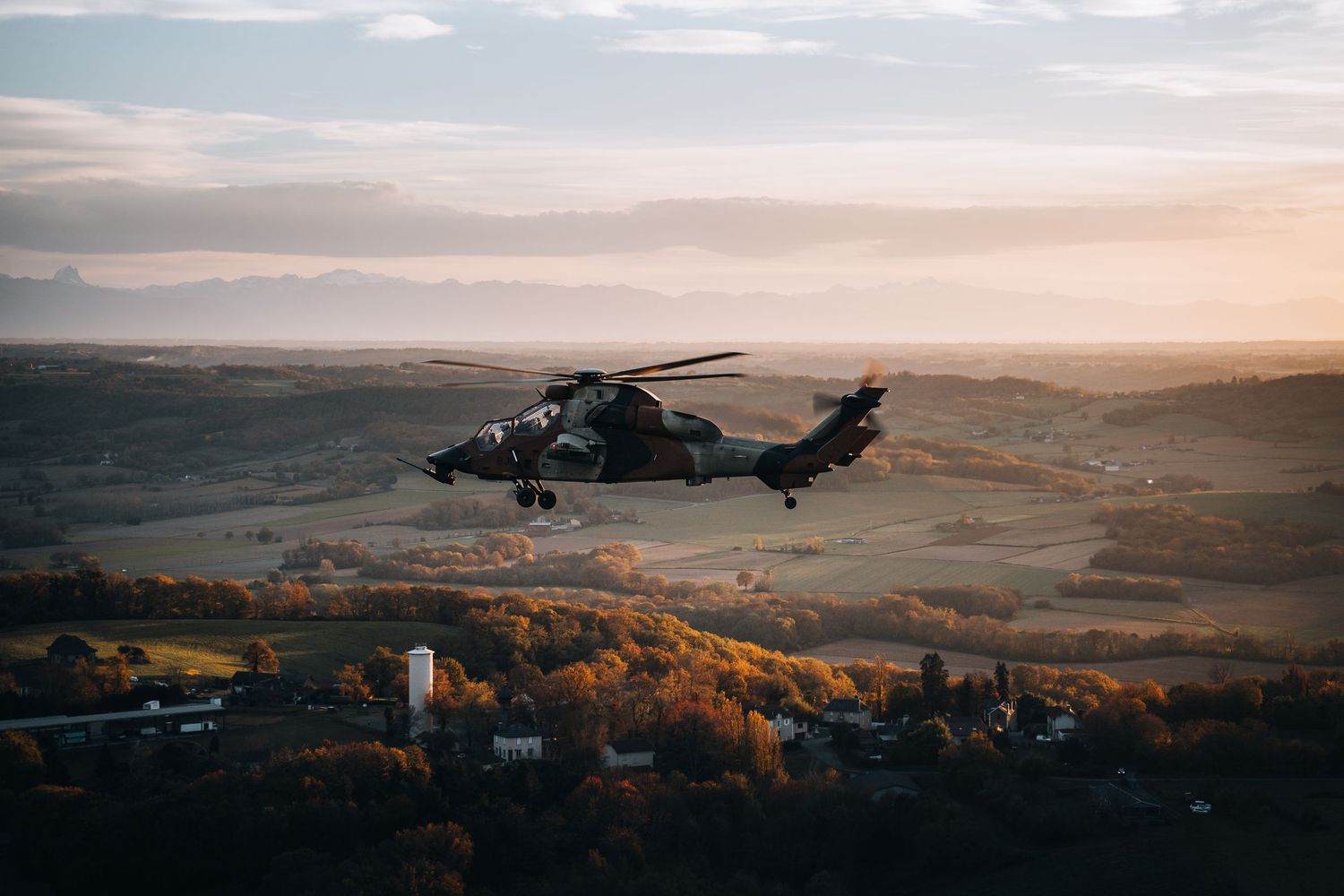 Military helicopter flying over a scenic autumn valley landscape at golden hour sunset.