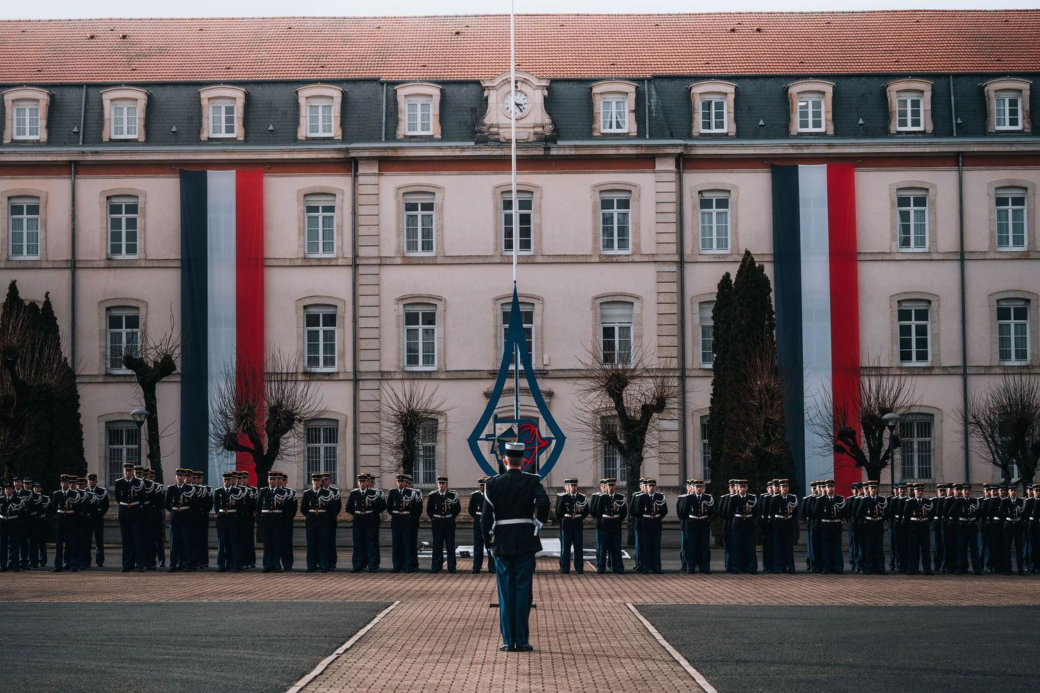 Military ceremony with soldiers lined up before a building decorated with red and white national flags.