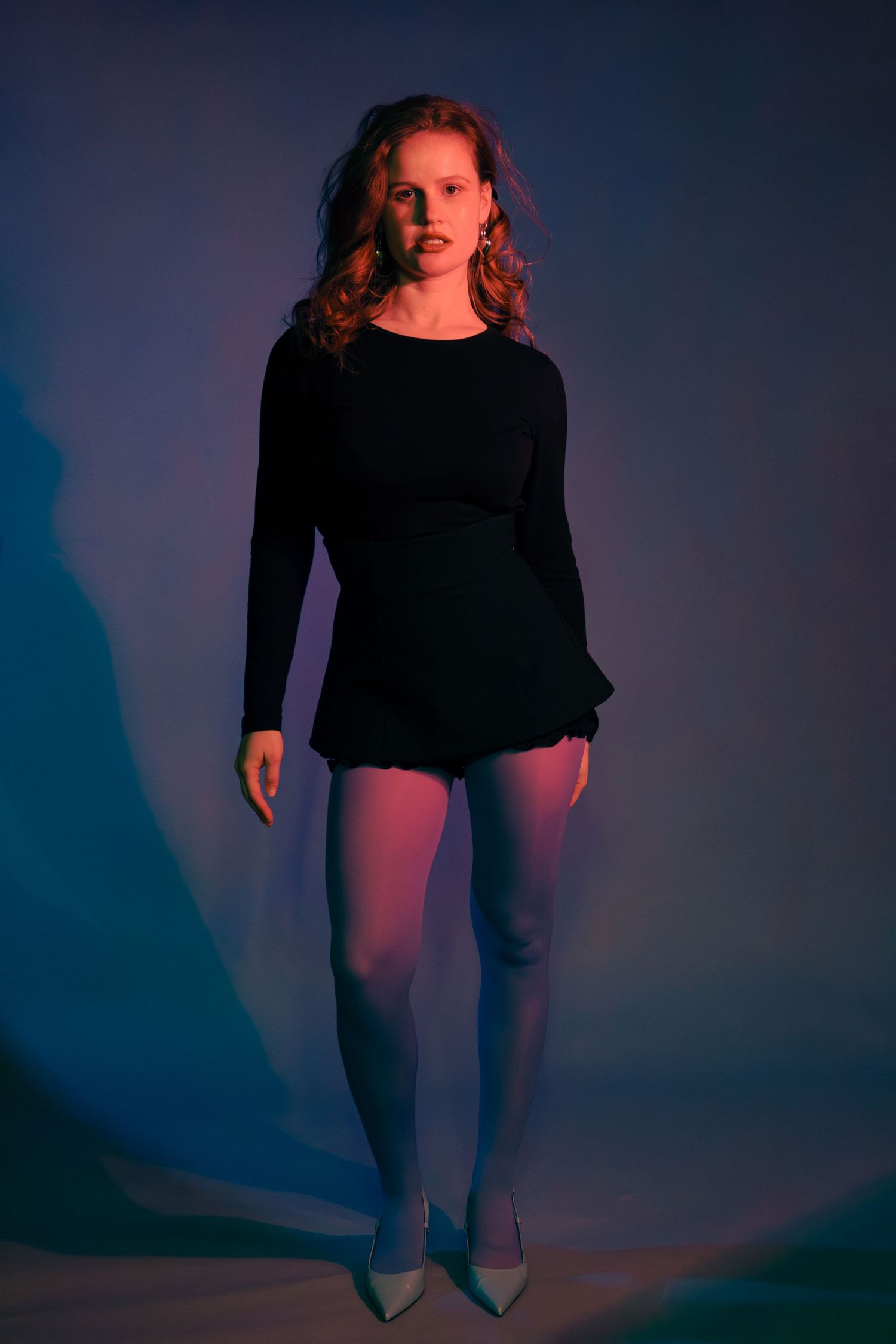 Woman in black mini dress and tights under colorful studio lighting.