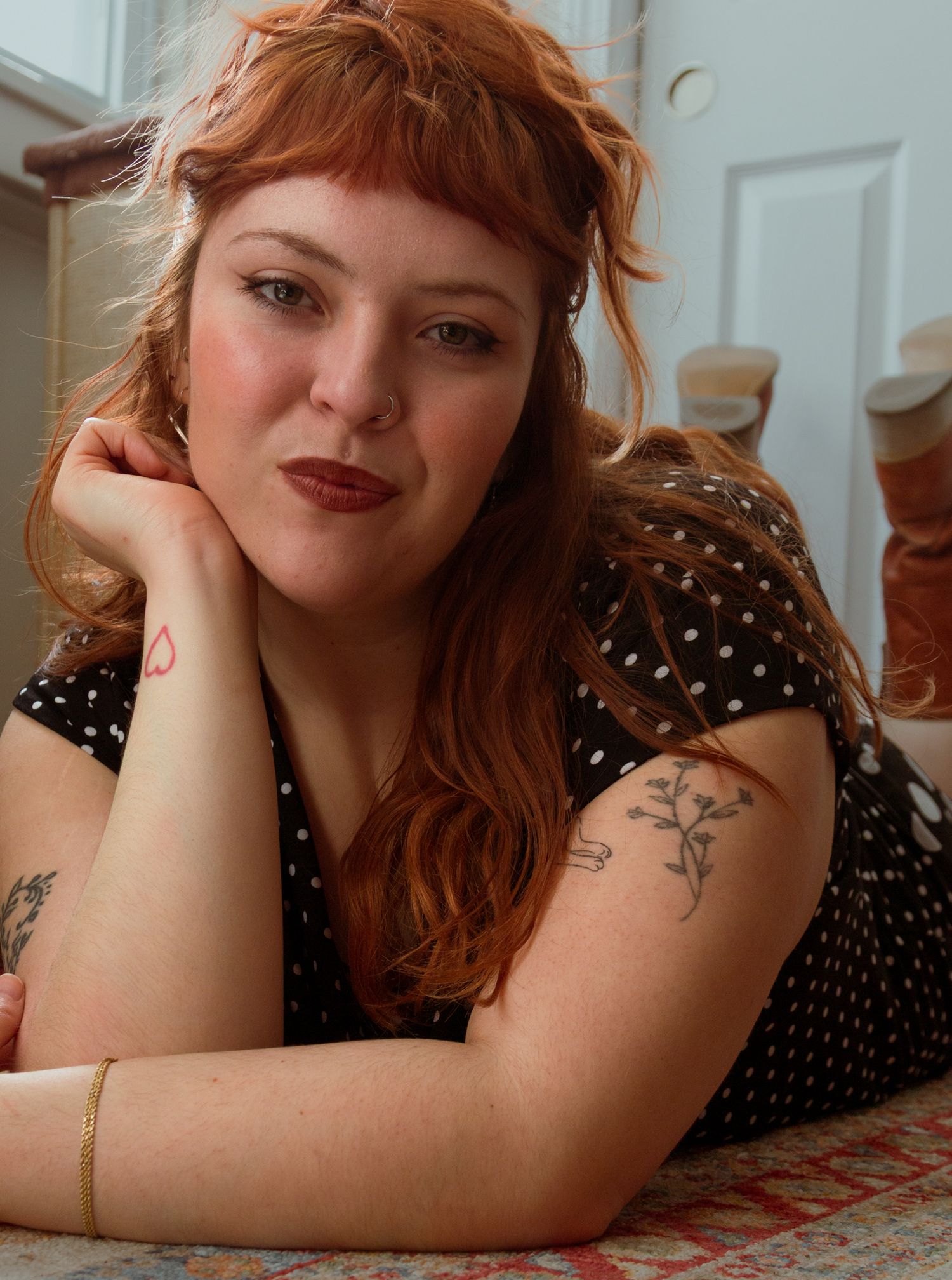 Redhead woman with tattoos lying down in polka dot dress.