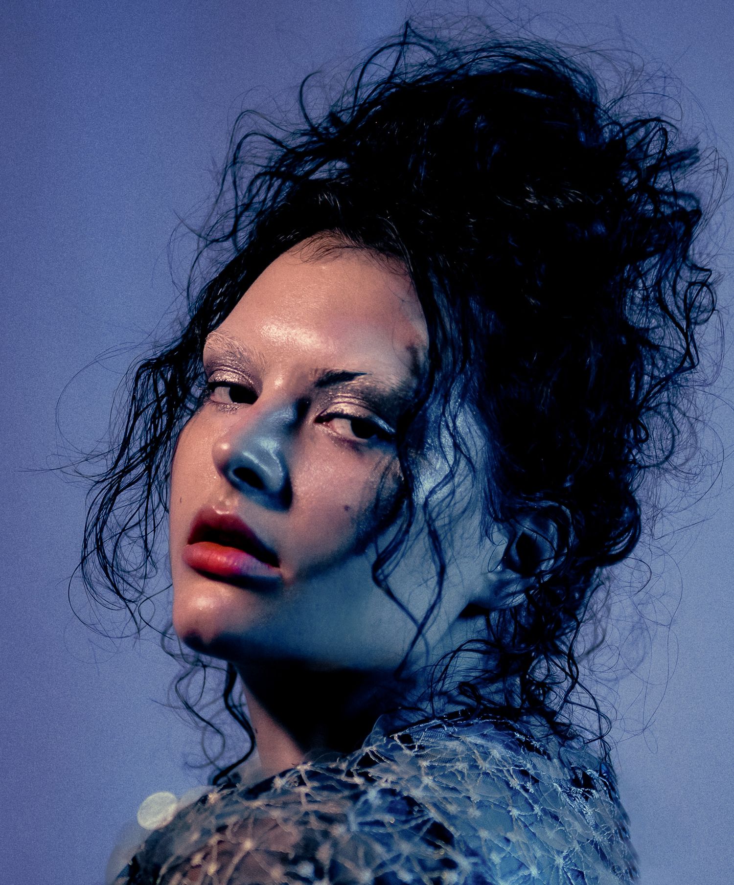 Woman with dark curly updo and red lips under blue dramatic lighting.