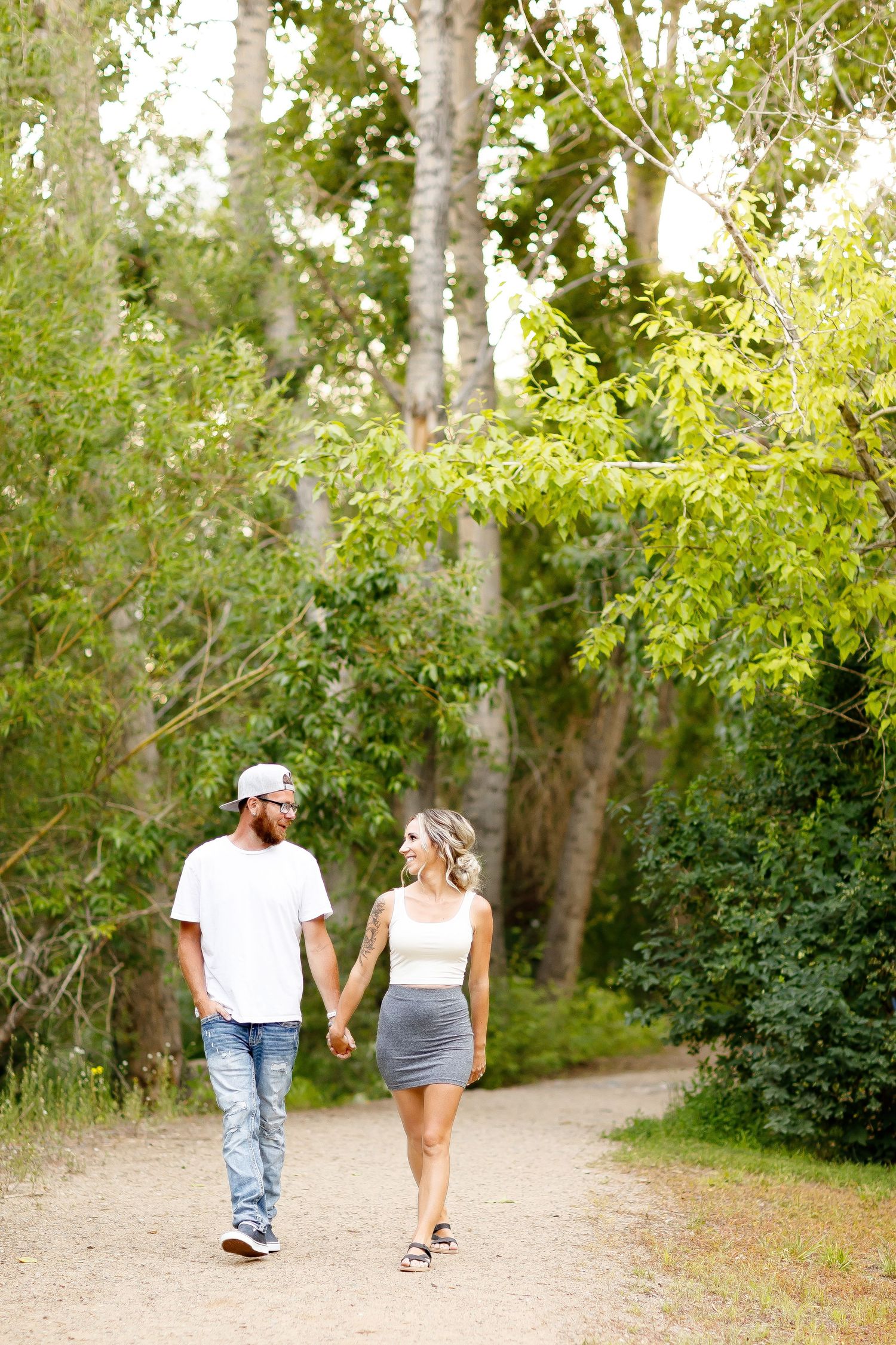 Happy couple walking hand in hand along a tree-lined dirt path during engagement photos.