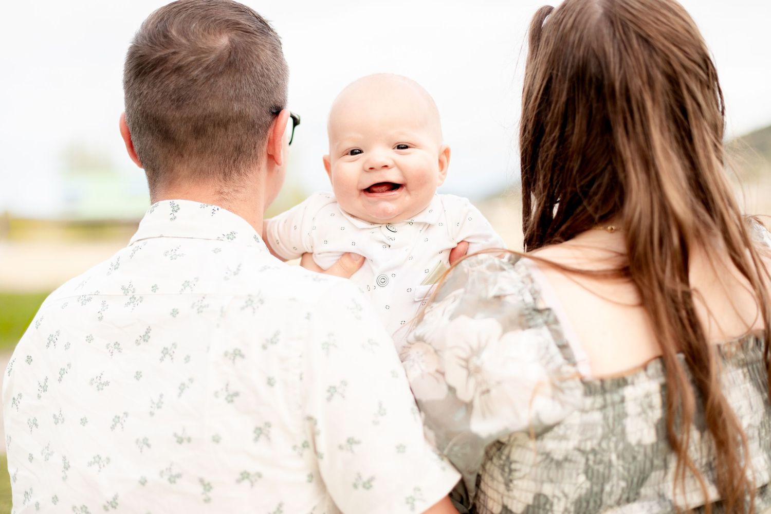 Baby smiling over fathers shoulder at parents during outdoor family photography session.