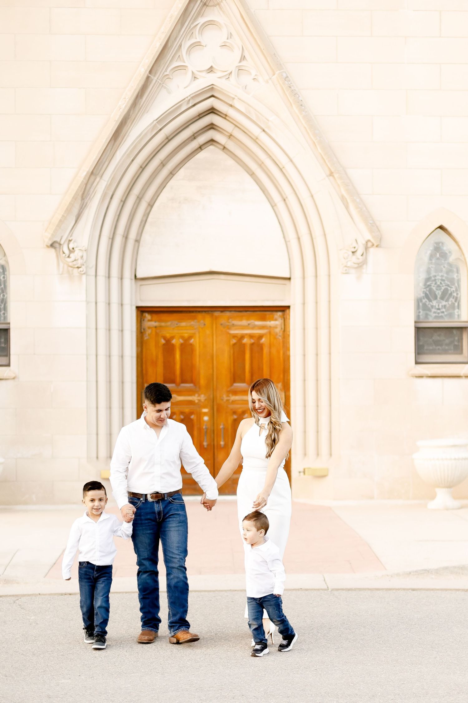 A family of four holds hands and walks in front of a grand church entrance with arched doors.