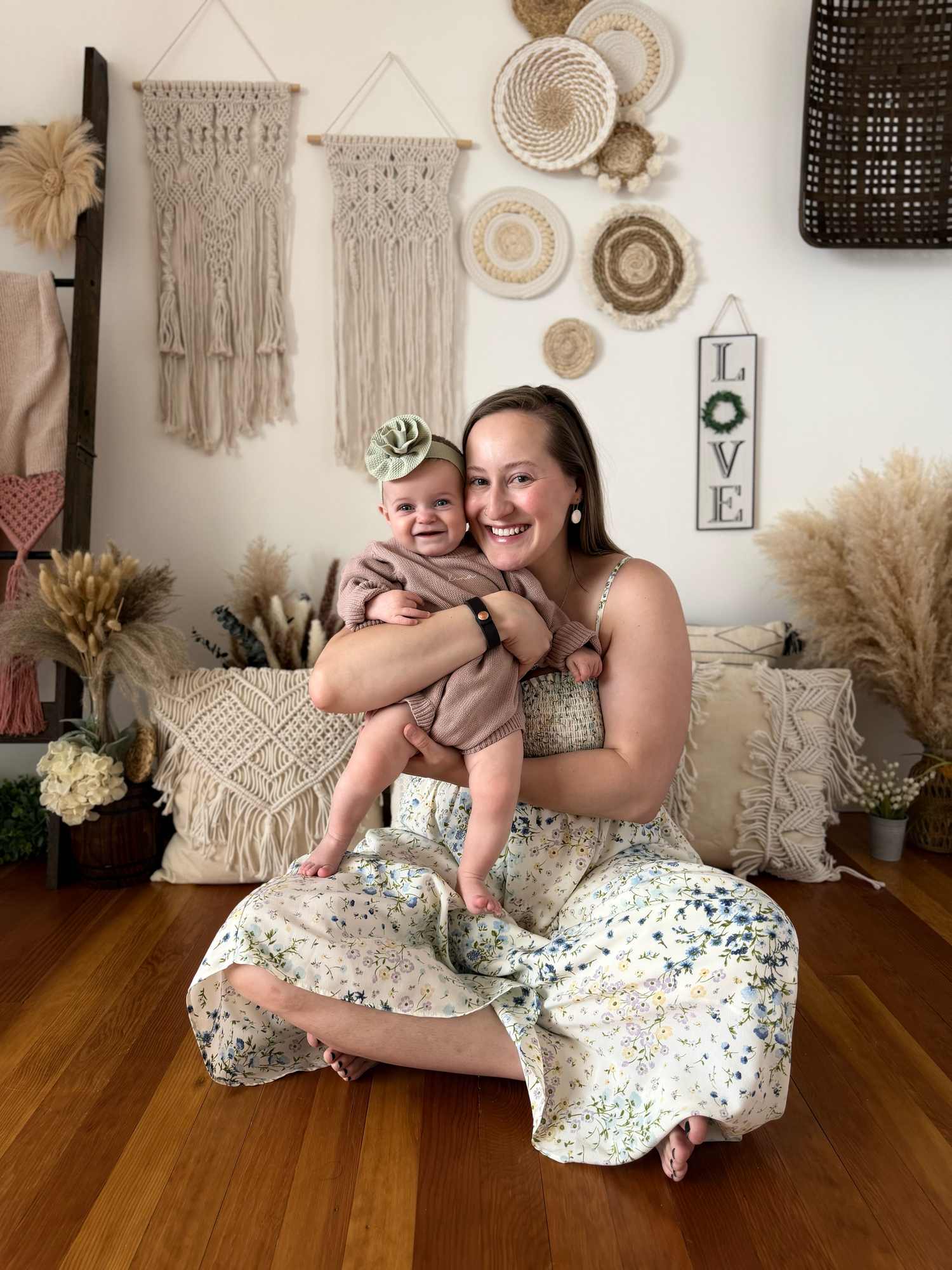 Joyful mother holding infant in bohemian styled studio with macrame hangings and LOVE sign.