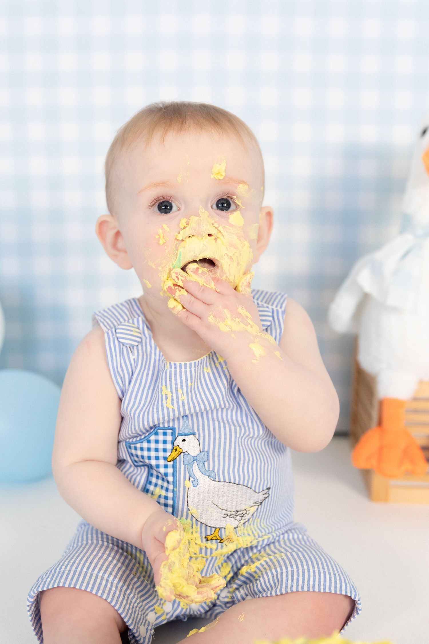 Baby with yellow cake smashed on face eating with hand during first birthday cake smash photo session.