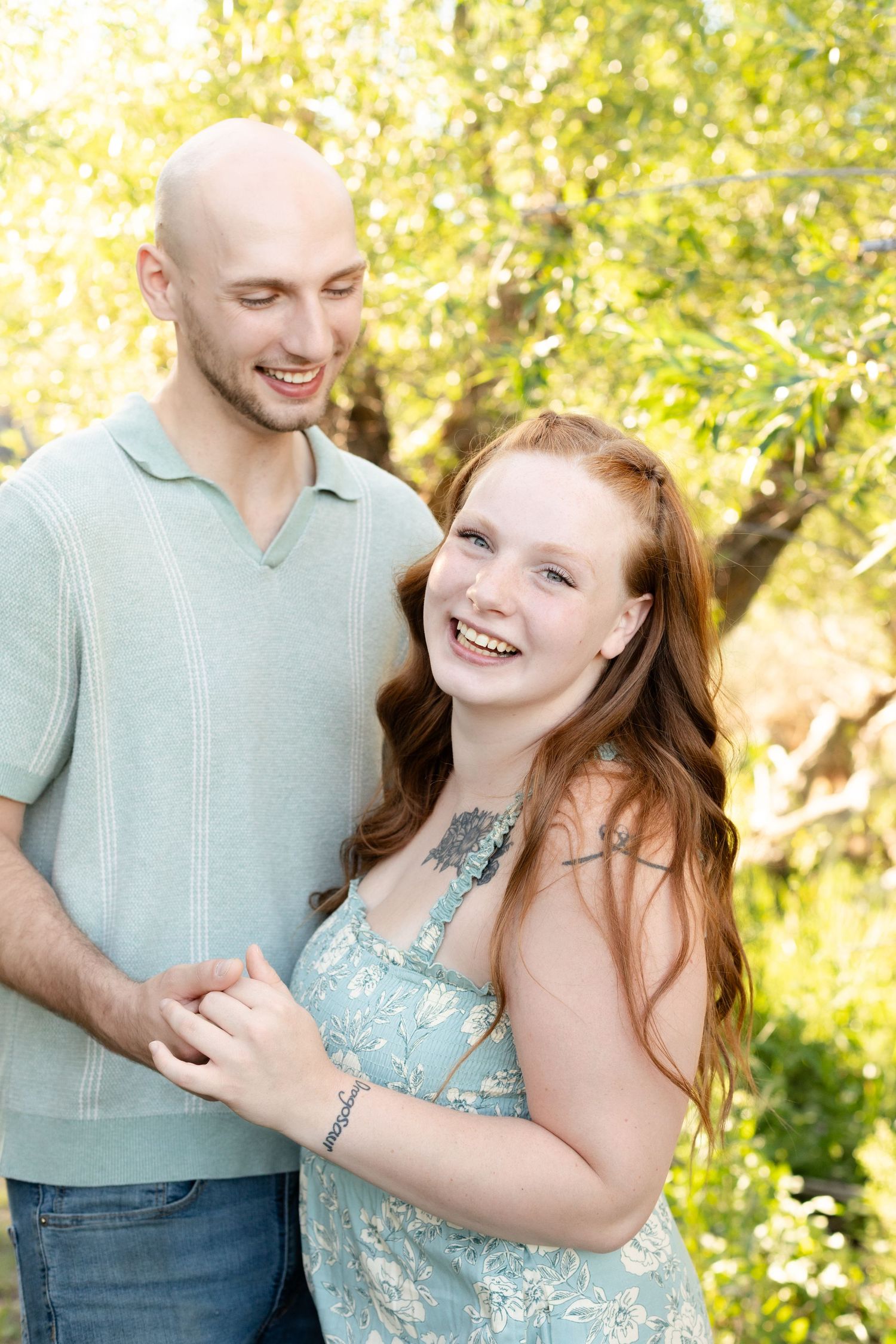Laughing redhead woman and bald man holding hands in a bright sunlit outdoor setting.