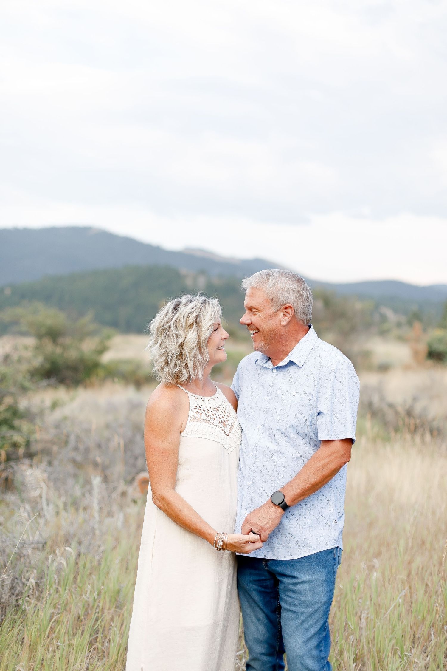 Mature couple holding hands and gazing at each other in a scenic mountain meadow.