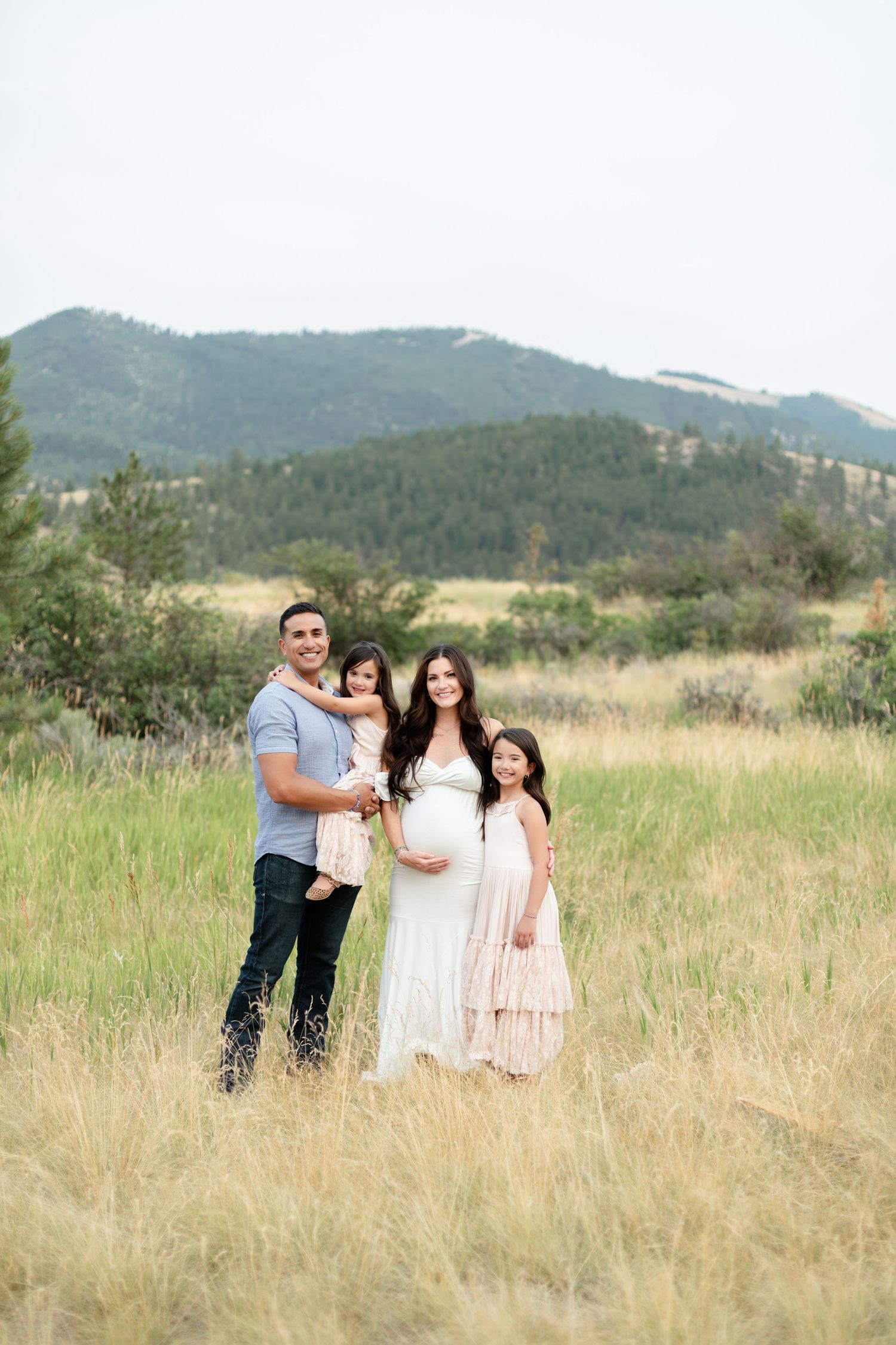Happy family maternity photo with pregnant mom in white dress in mountain meadow.