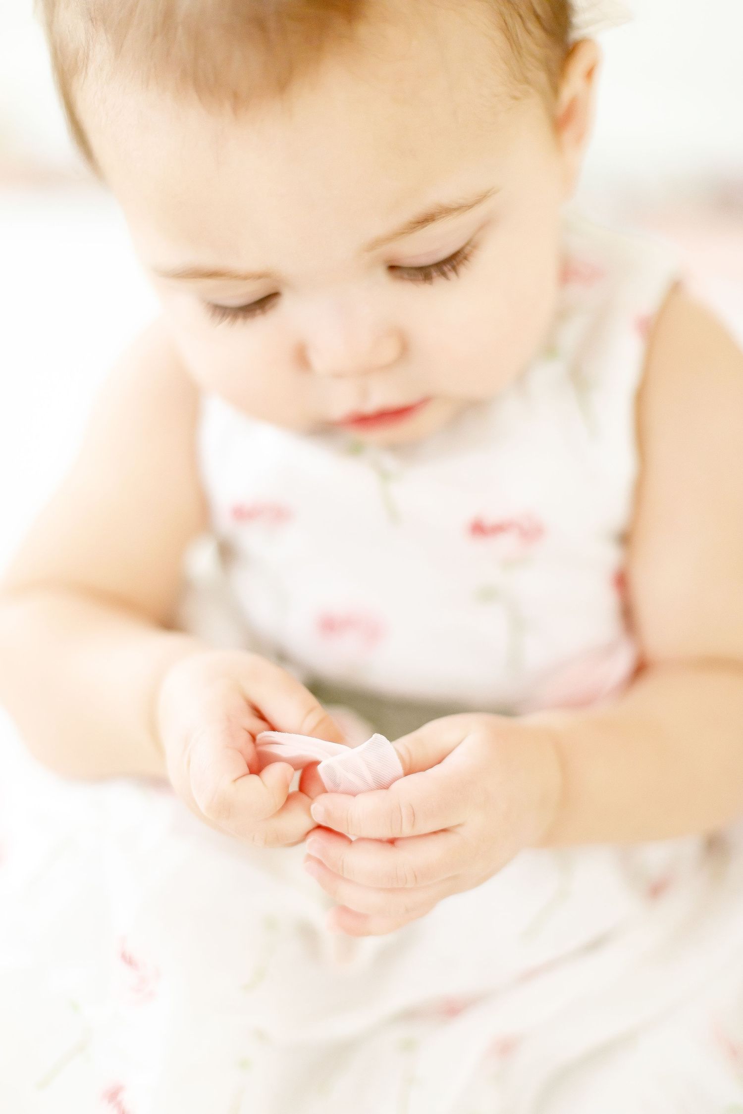 Adorable baby girl in floral dress looking down at hands during professional portrait session.