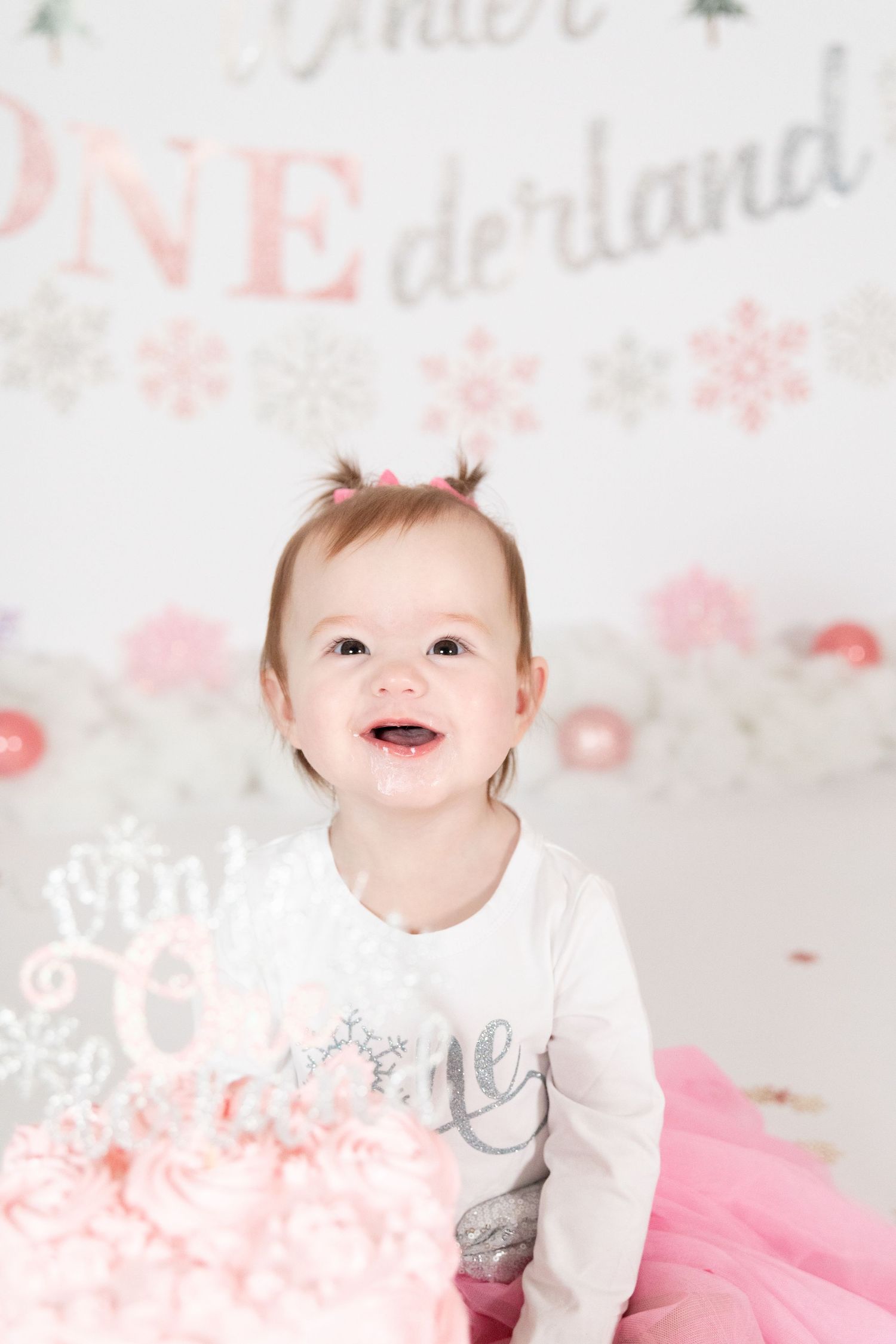 Smiling baby girl in pink tutu with pink birthday cake at Winter ONEderland first birthday party.