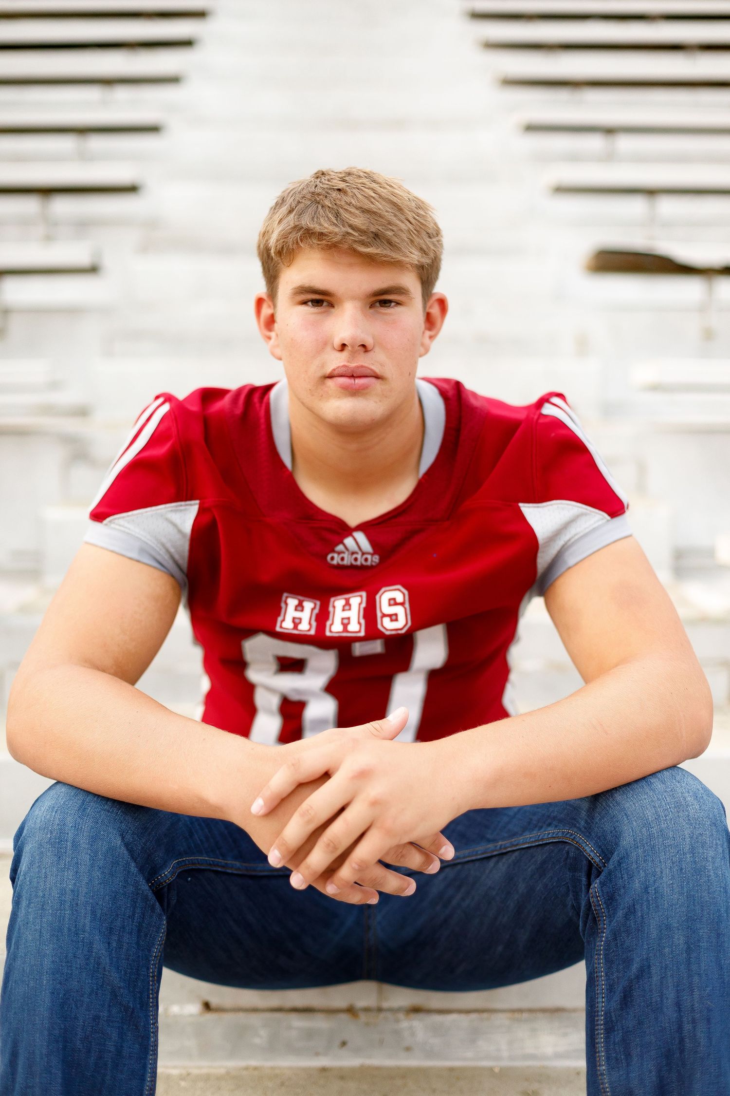 A high school football player in a red HHS jersey sits confidently on bleacher steps outdoors.