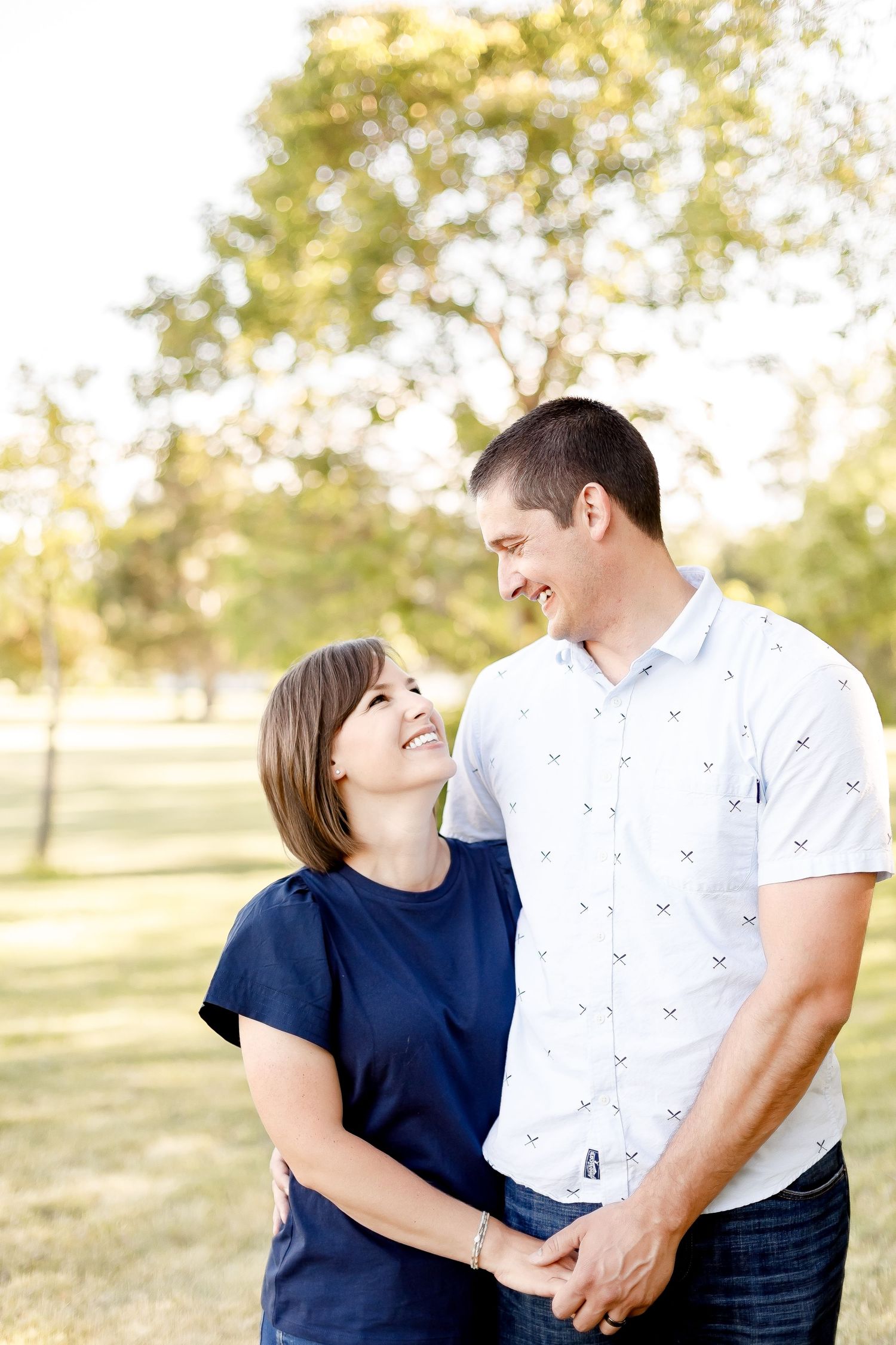 Happy couple holds hands and gazes at each other lovingly in a sunny park.