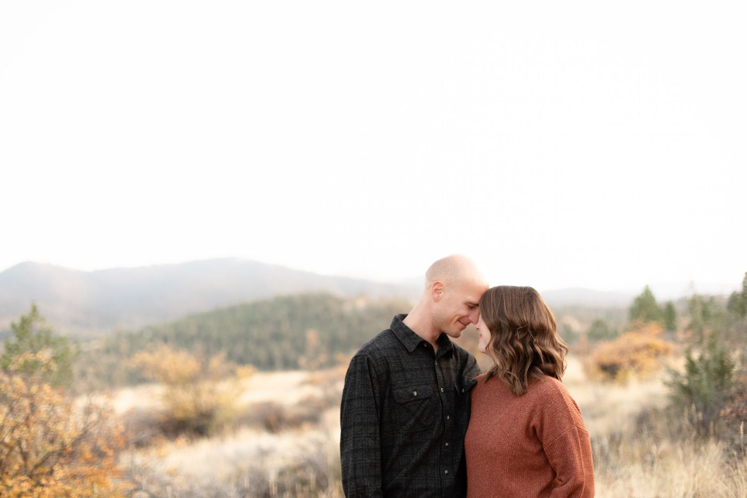 Romantic couple touching foreheads in a golden autumn field with mountain landscape behind them.