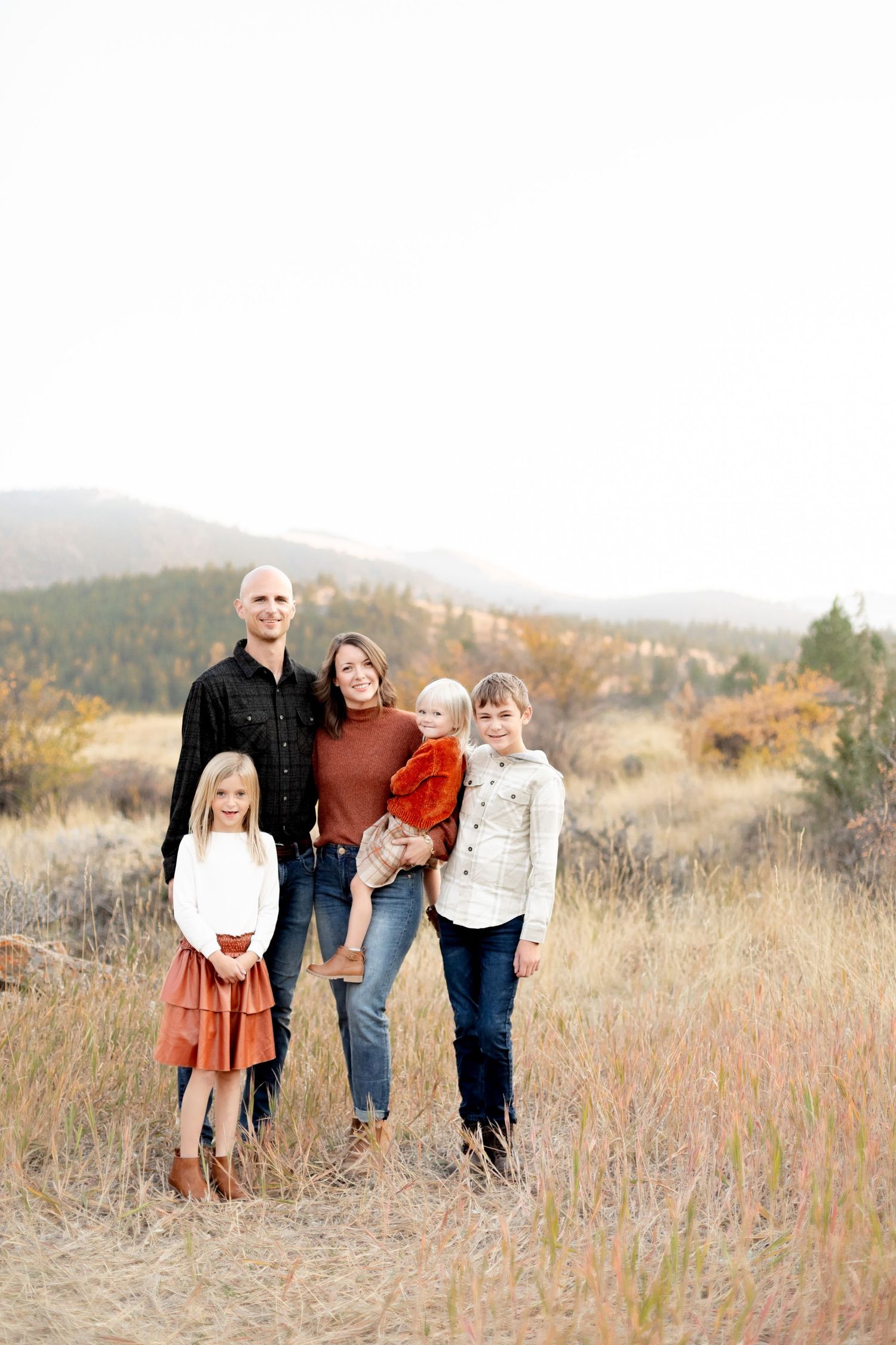 Family of five posing together in an autumn mountain meadow with colorful fall foliage backdrop.