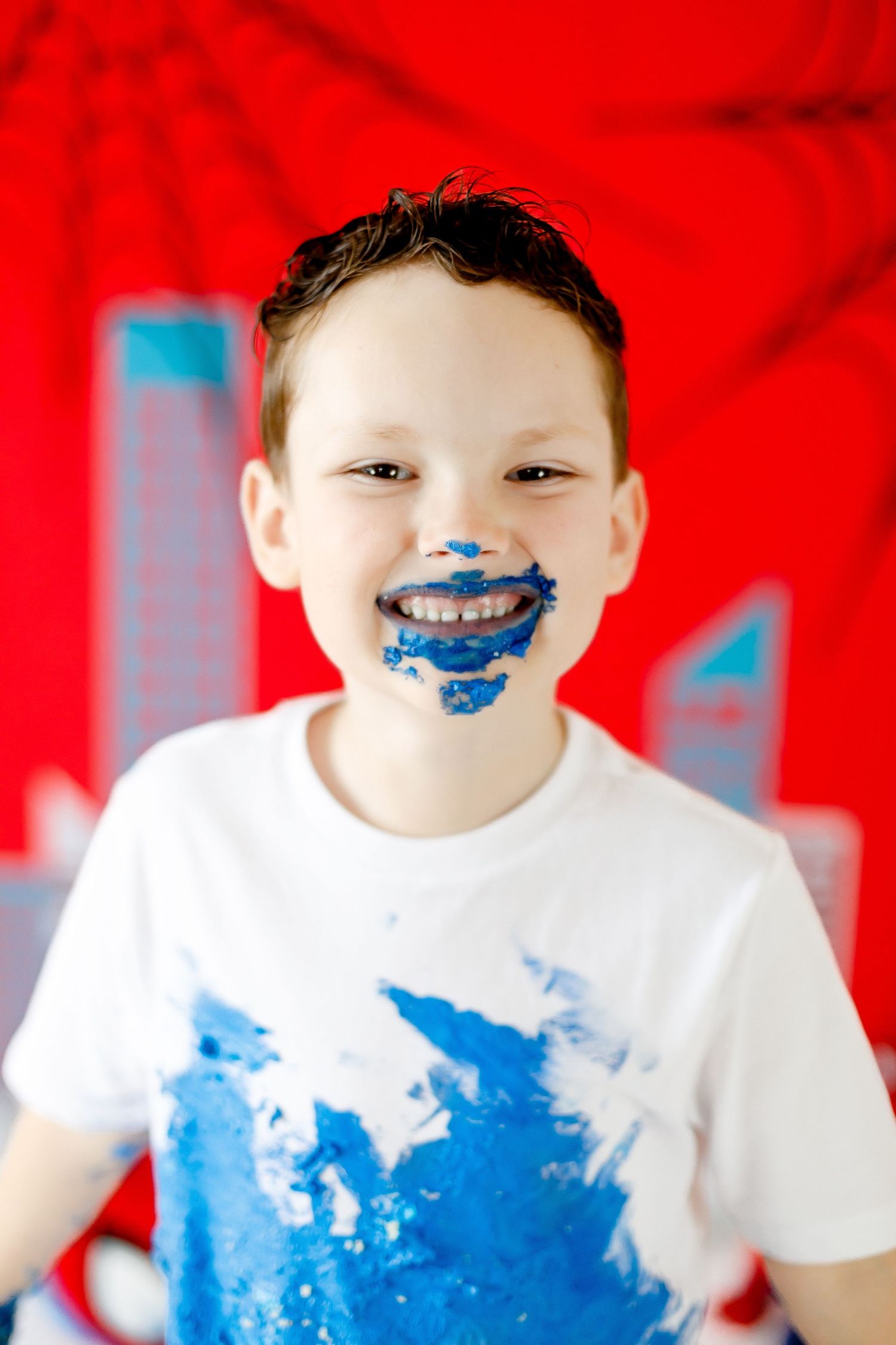 A smiling boy with blue frosting on his face poses at a Spiderman-themed birthday party.