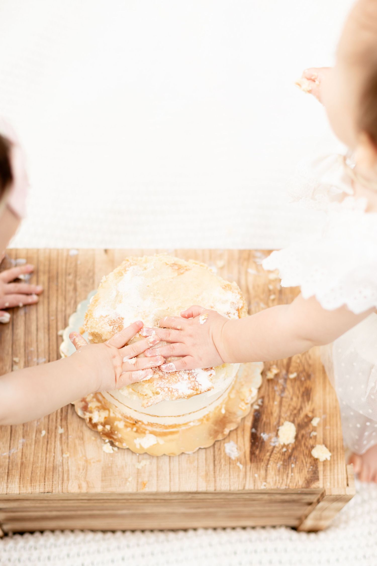 Overhead view of two babies hands smashing a first birthday cake together on a wooden table.