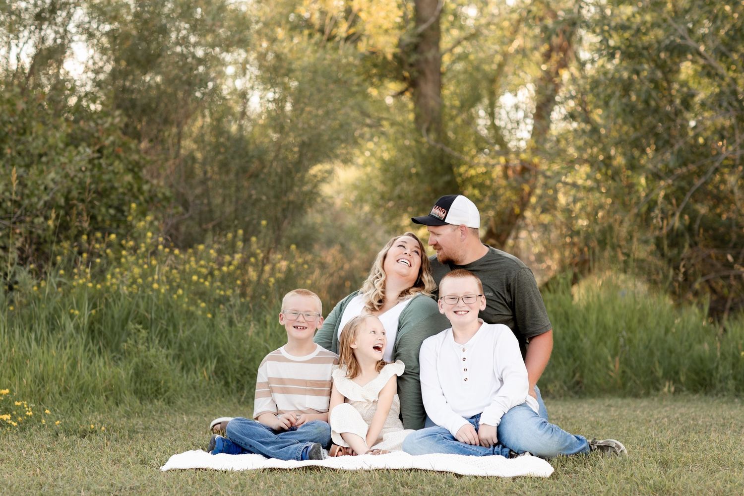 Joyful family of five laughing together on a blanket in a sunny green meadow.
