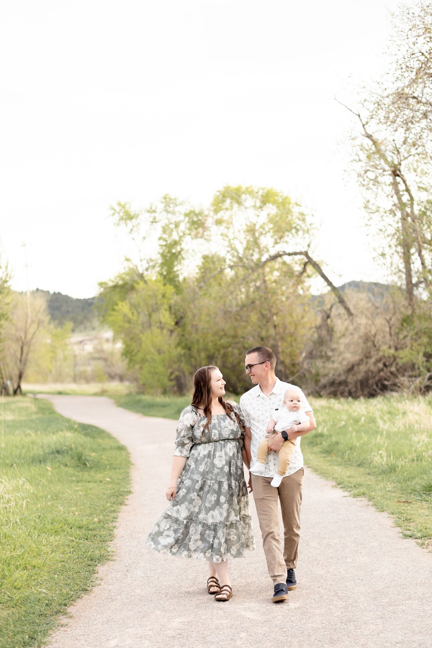Young family with baby strolling on a winding park path surrounded by spring greenery.