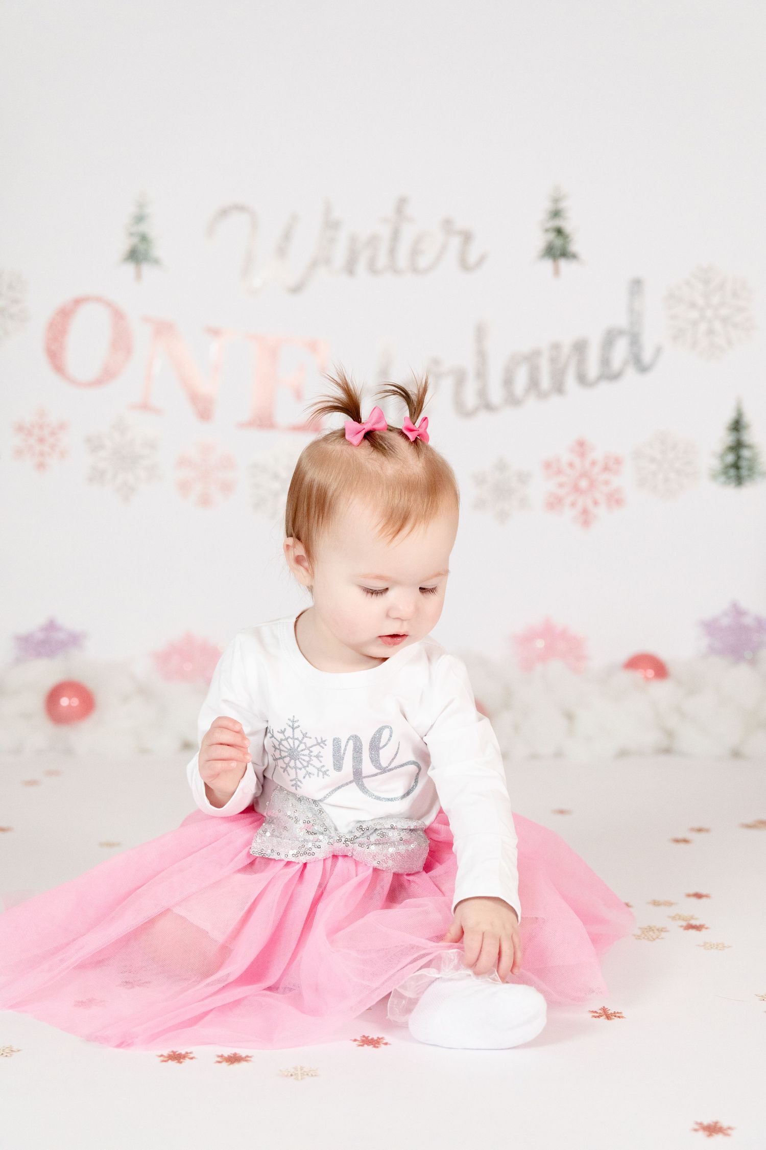 Baby girl in pink tutu and white one shirt playing at Winter ONEderland first birthday setup.