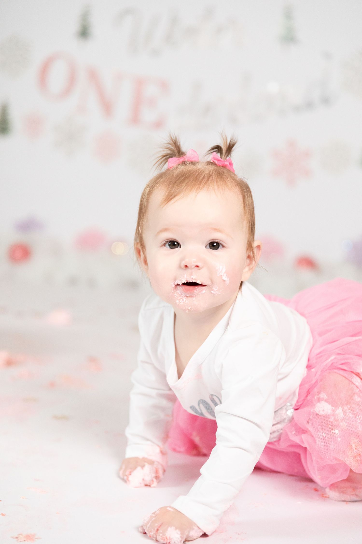 Baby girl in pink tutu with cake on her face crawling during Winter ONEderland first birthday cake smash.