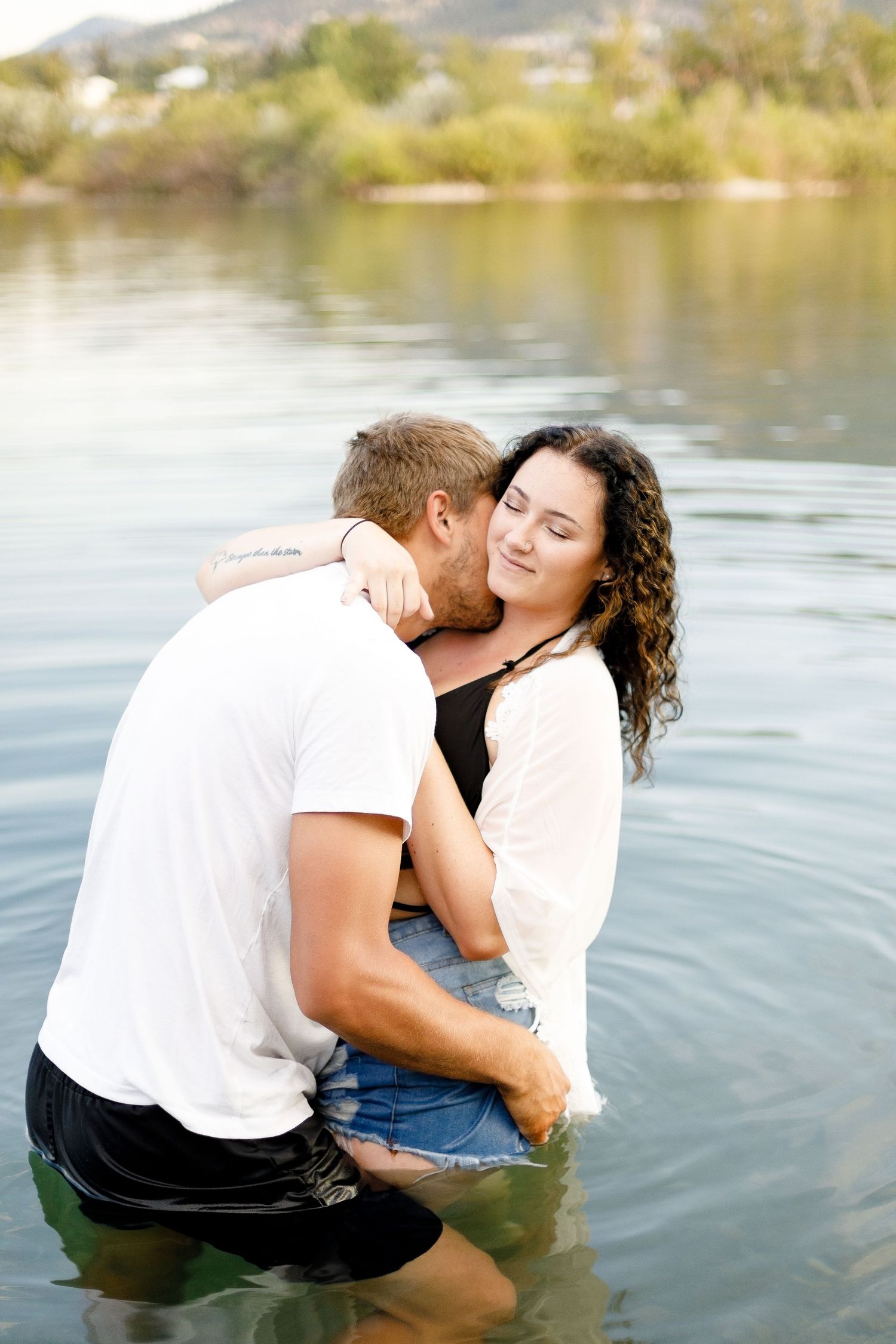 Couple sharing a tender kiss while standing together in a lake with scenic mountain views.