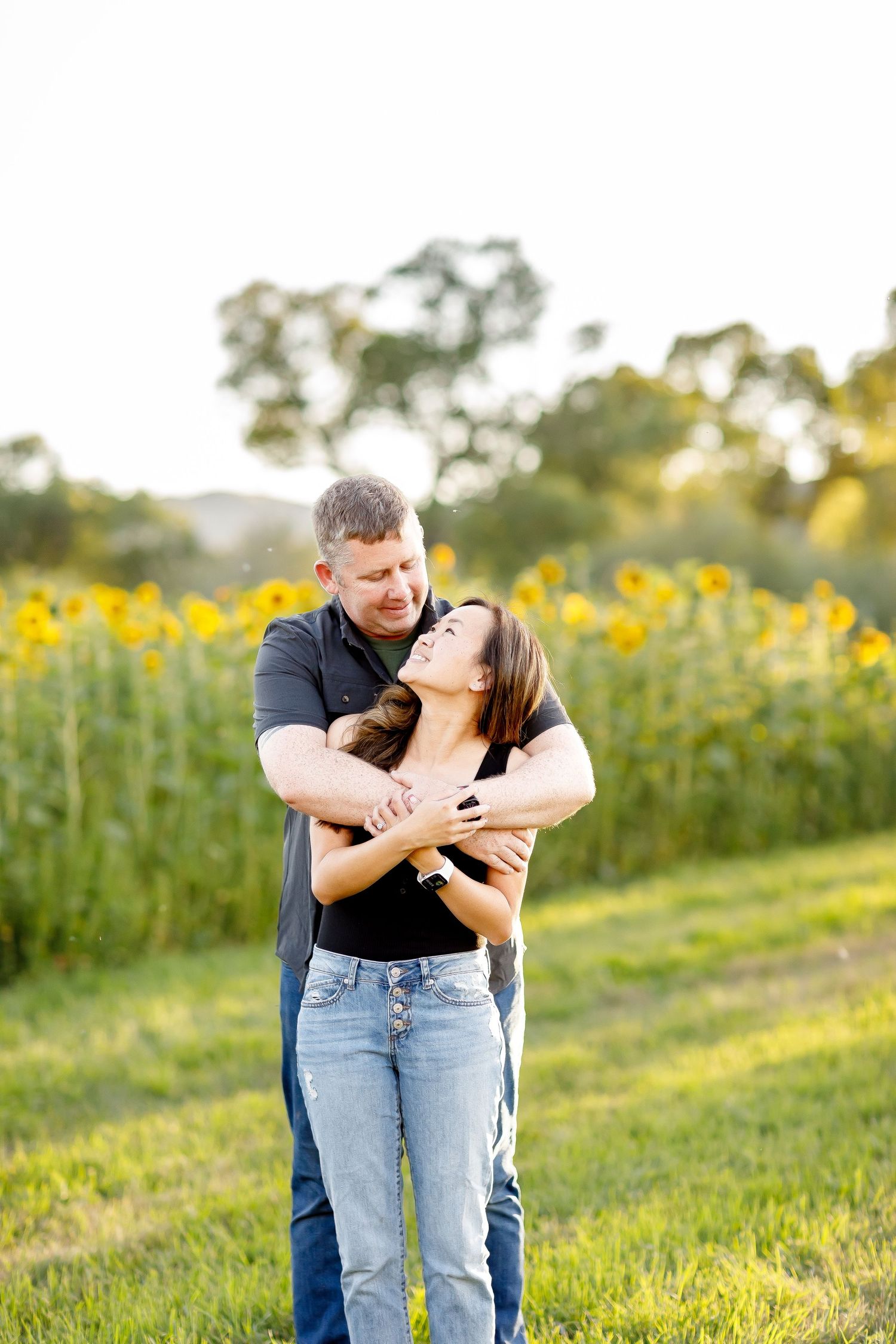 Couple sharing a tender embrace in front of a vibrant sunflower field during a romantic outdoor engagement session.