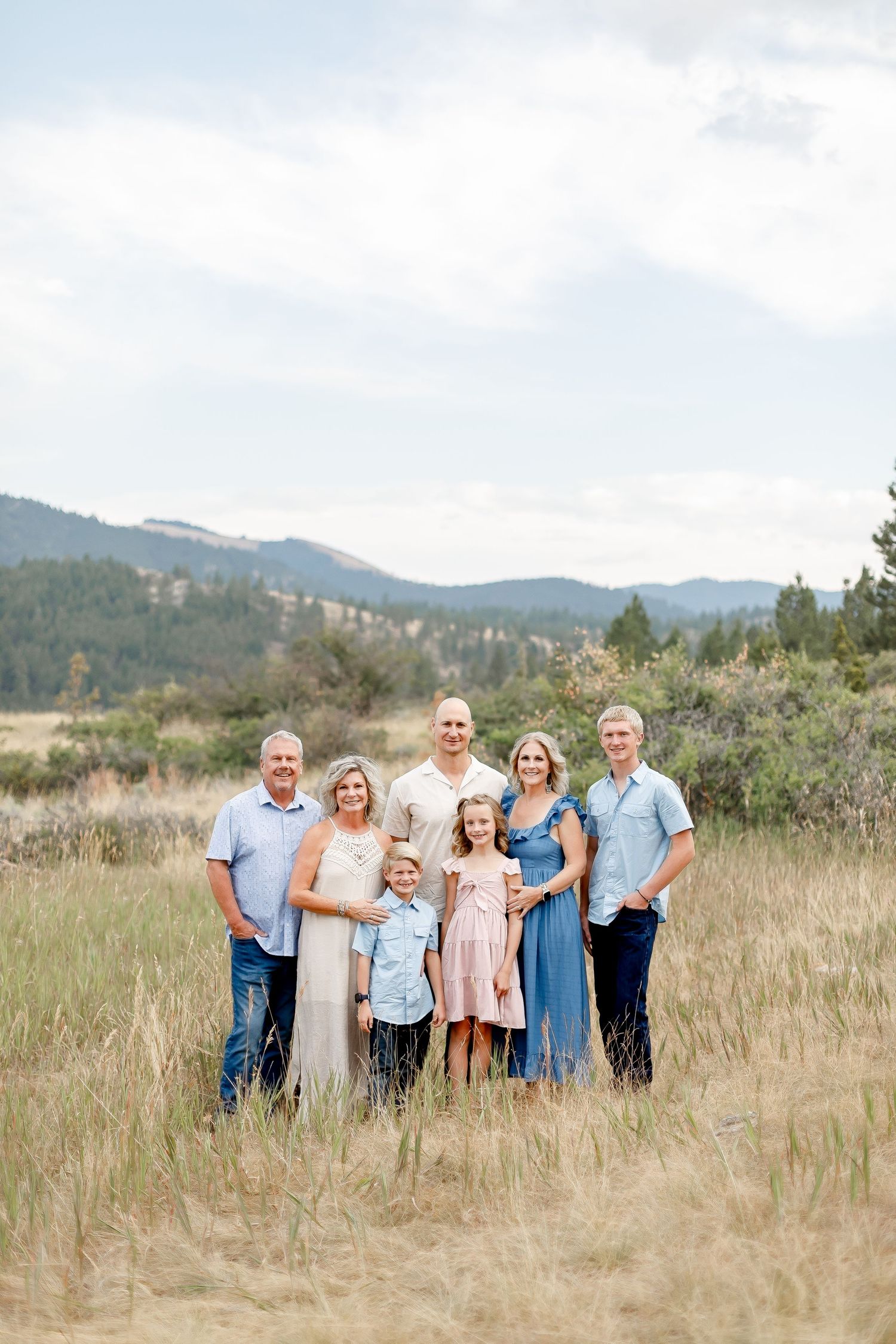 Extended family of seven posing together in a wide mountain meadow on a cloudy day.