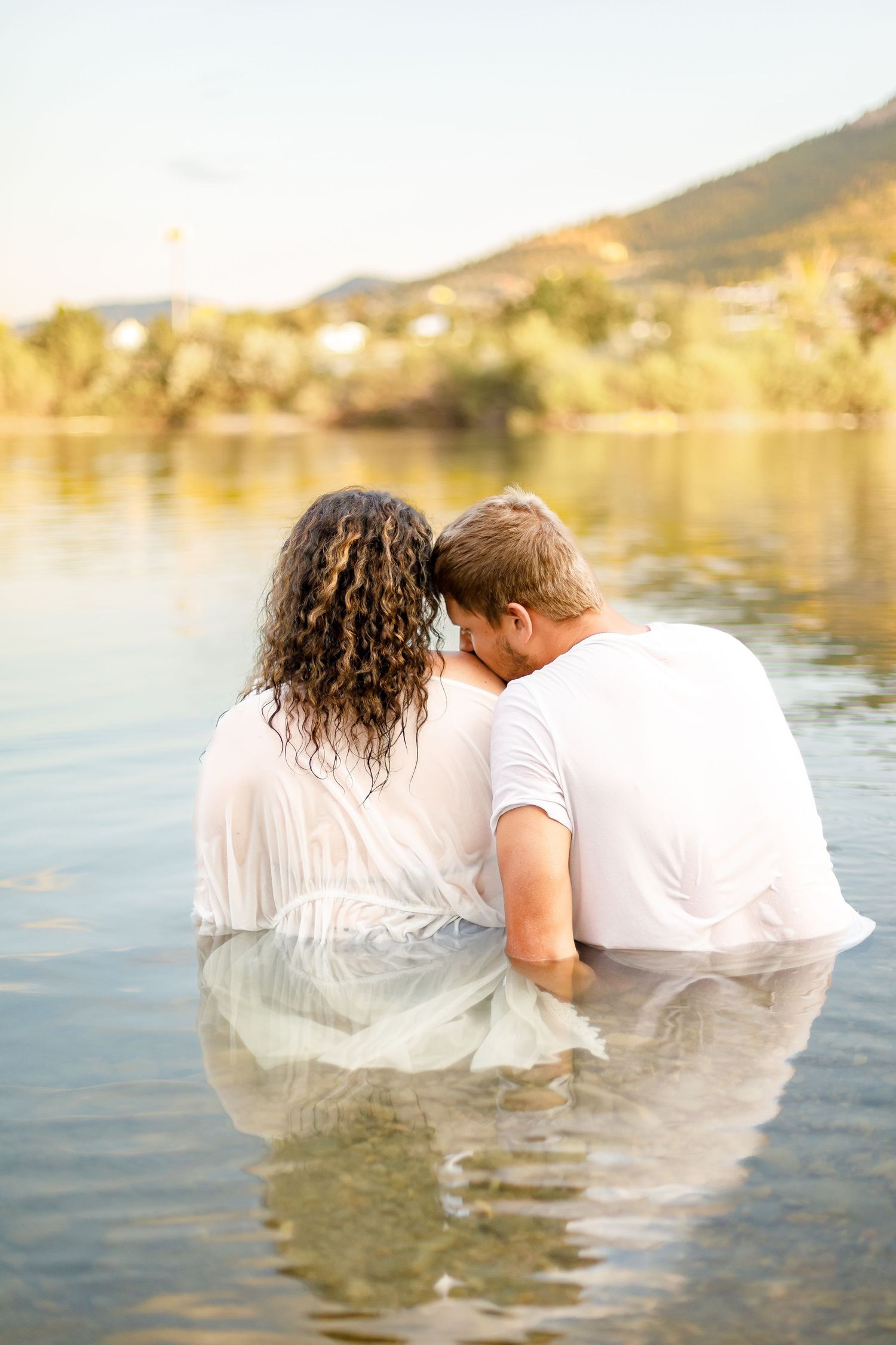Romantic couple sitting close together in a lake with their foreheads touching at golden hour.