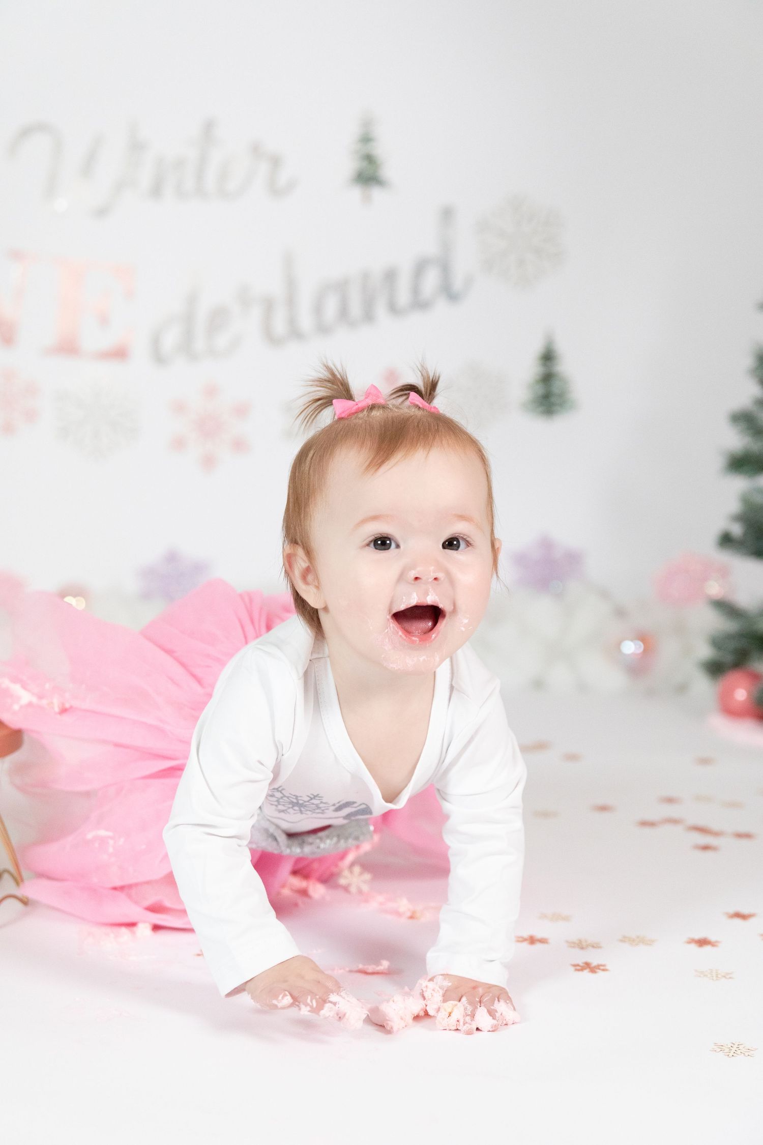 Laughing baby girl in pink tutu crawling during Winter ONEderland first birthday cake smash photoshoot.