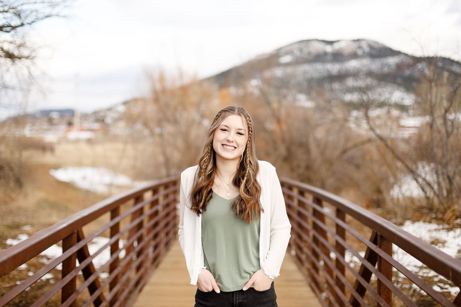 Laughing teenage girl in white cardigan and green top standing on a wooden bridge in winter.