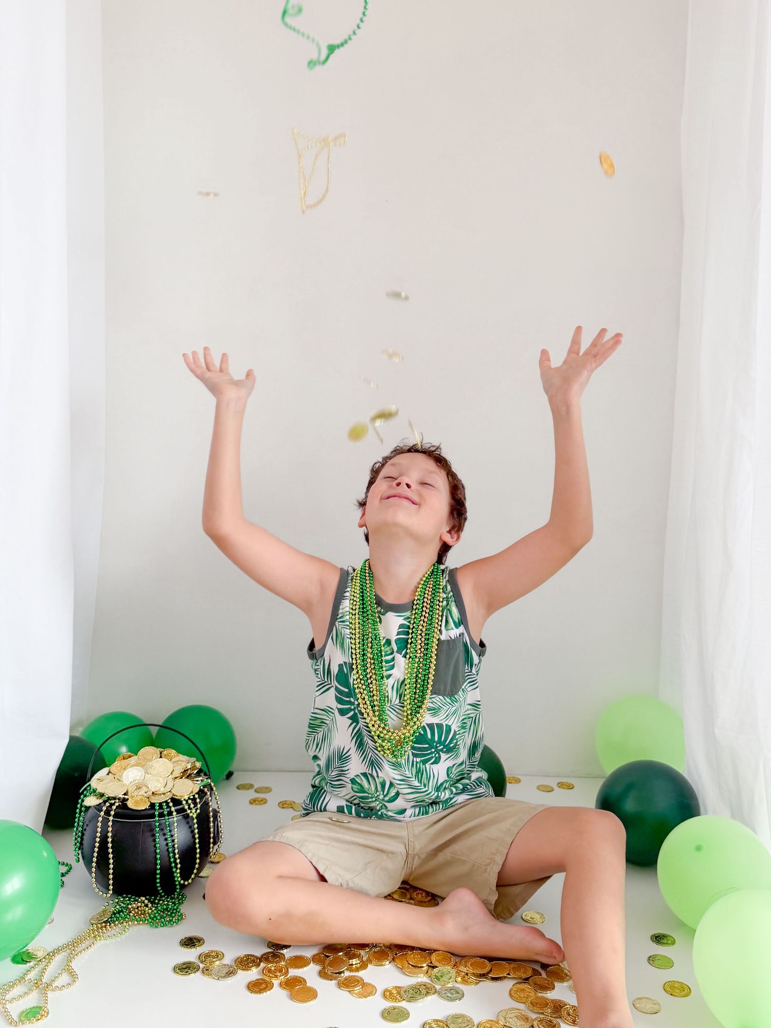 Excited boy tossing gold coins and streamers with St. Patrick's Day balloons and decorations.