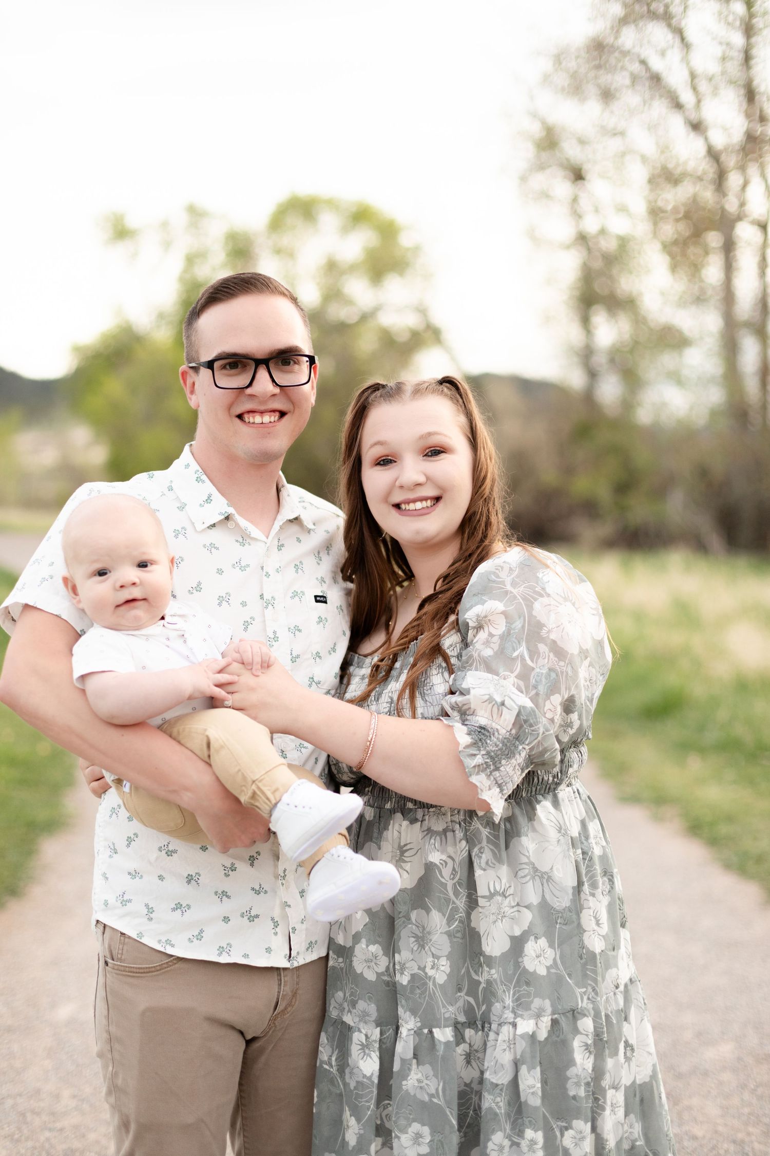 Young couple holding baby smiling on a park path during outdoor family photo session.