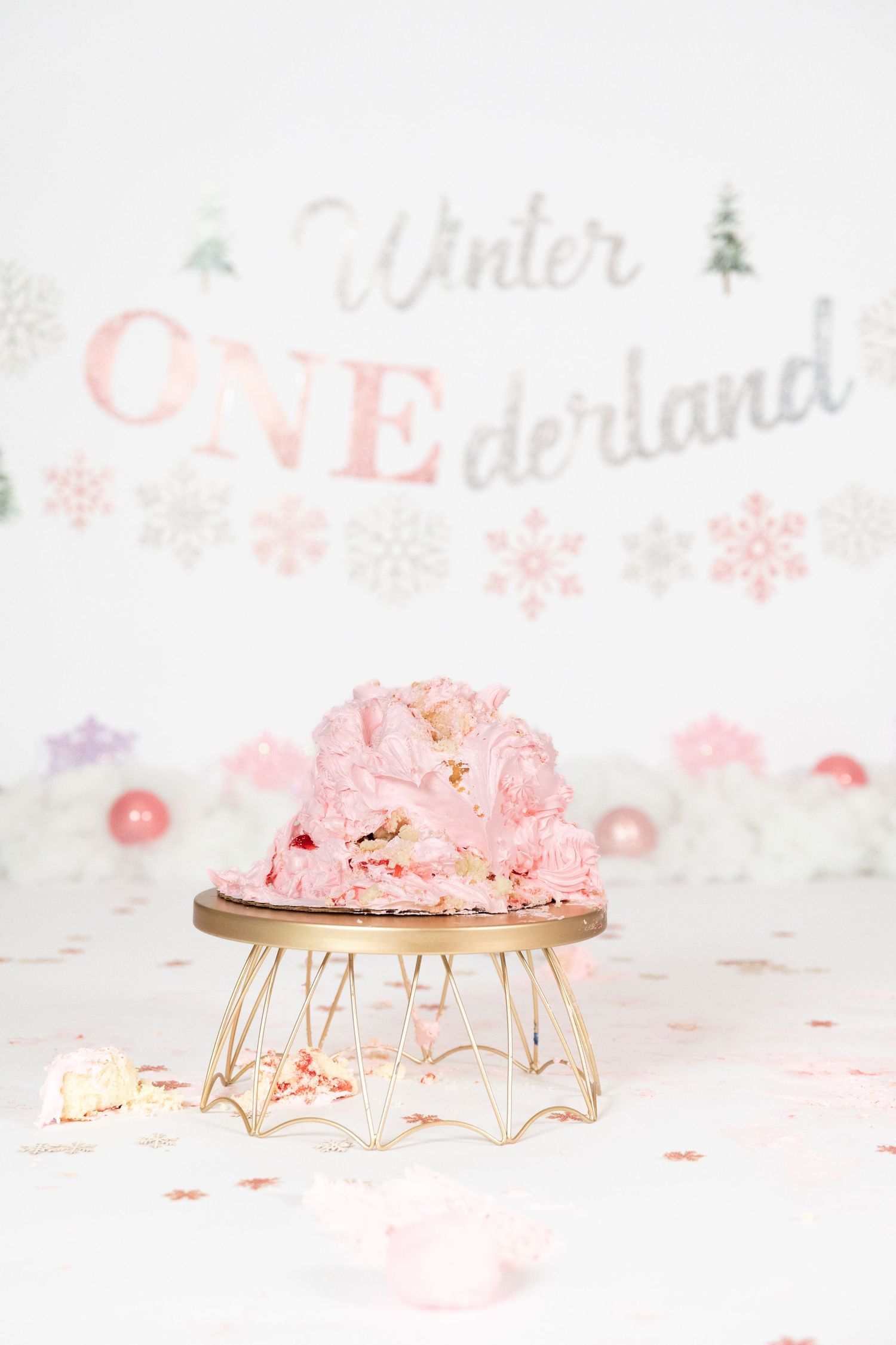 Smashed pink rosette first birthday cake on gold stand with Winter ONEderland backdrop decoration.
