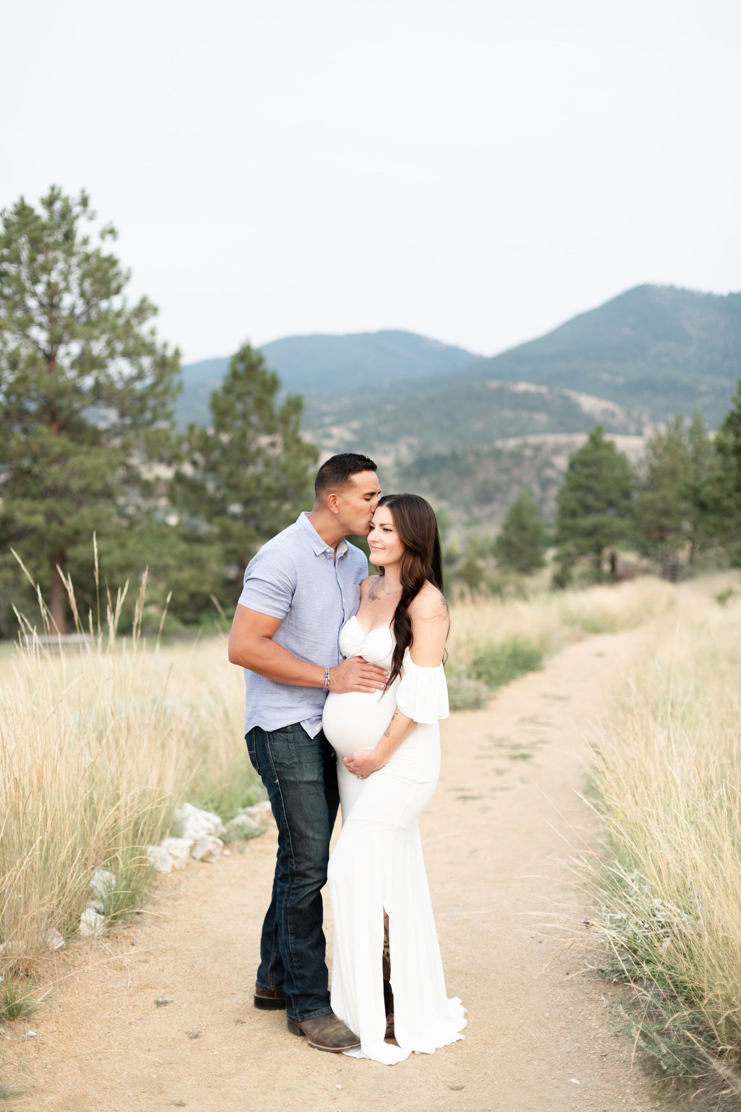 Couple sharing tender kiss during outdoor maternity photoshoot in mountain landscape.